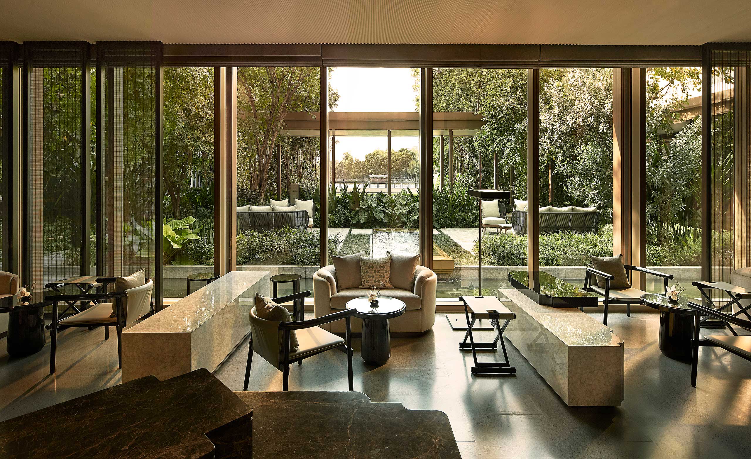 Luxurious hotel lounge with large windows overlooking a lush garden. Modern furniture and a serene ambiance create a peaceful, inviting atmosphere.