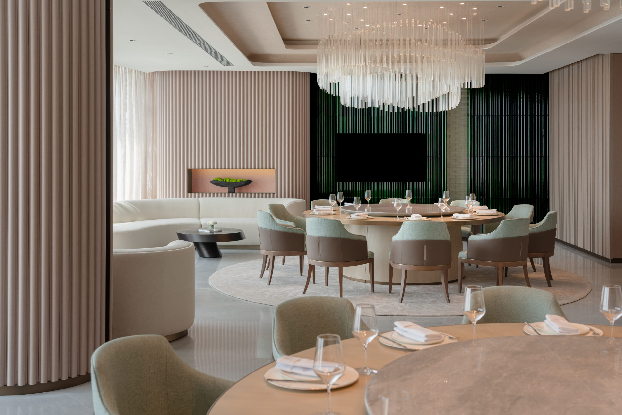 Elegant hotel dining room featuring a large round table with mint-green chairs, set for a meal. A modern chandelier hangs above, exuding a sophisticated ambiance.