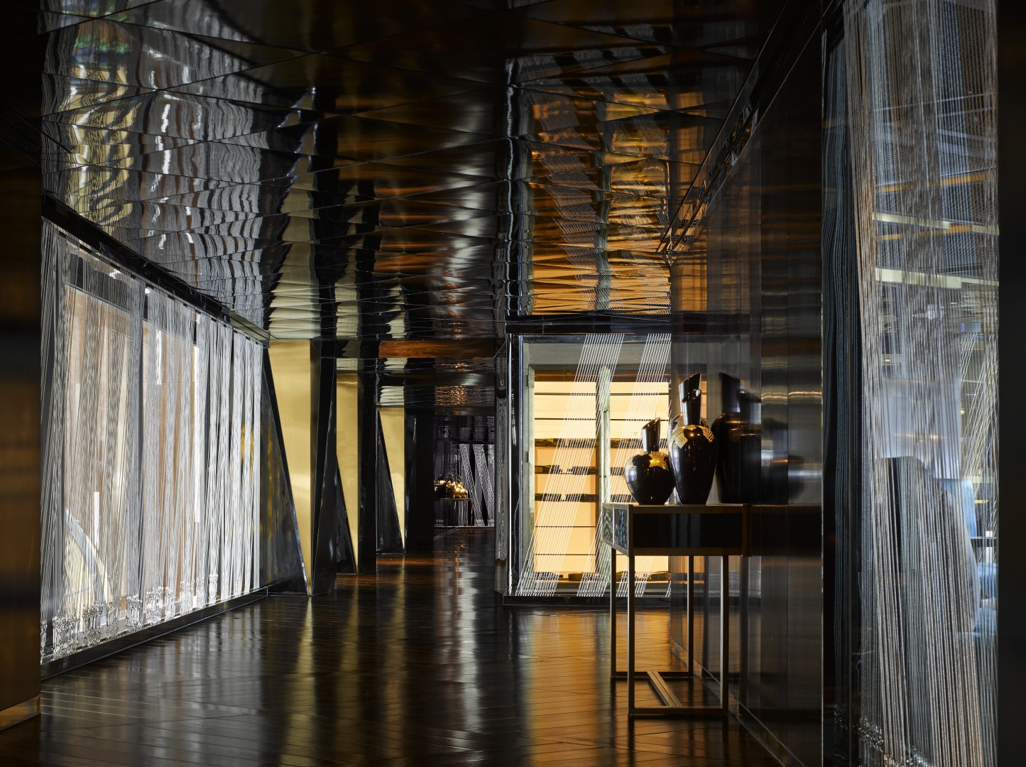 Dimly lit modern hotel hallway with reflective surfaces and intricate patterns. Soft warm light highlights pottery vases on a sleek table, creating an elegant ambiance.