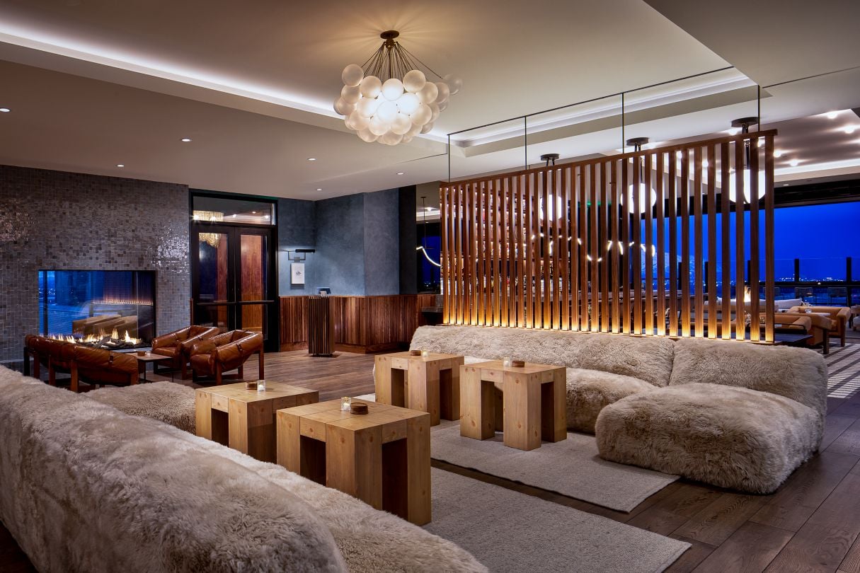 Elegant hotel lounge with plush beige sofas, wooden tables, and a modern fireplace. Chic lighting and wooden paneling create a cozy, sophisticated ambiance.