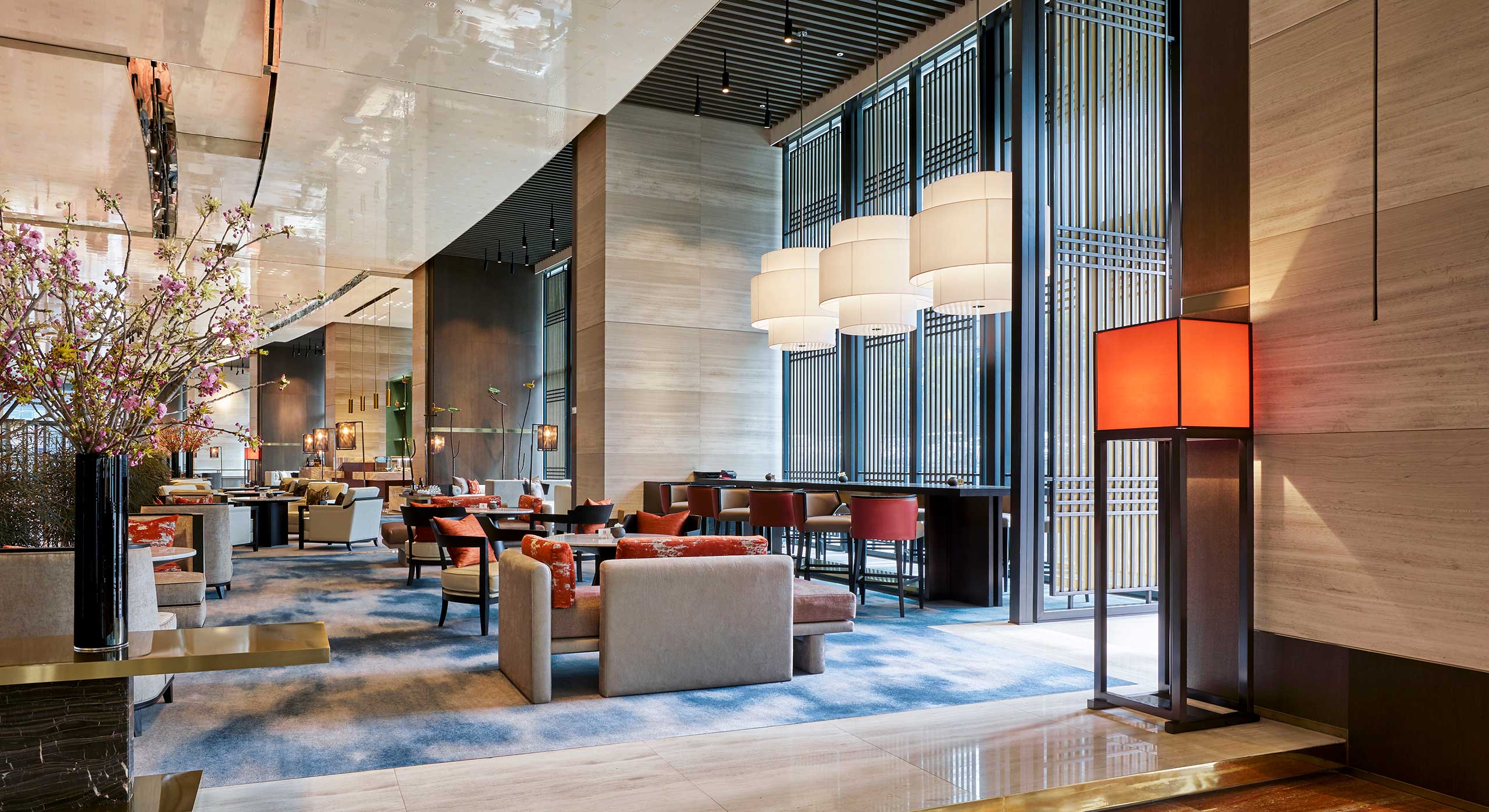 Elegant hotel lounge with modern decor: cream sofas, red chairs, large windows, and warm lighting. Inviting and luxurious ambiance.