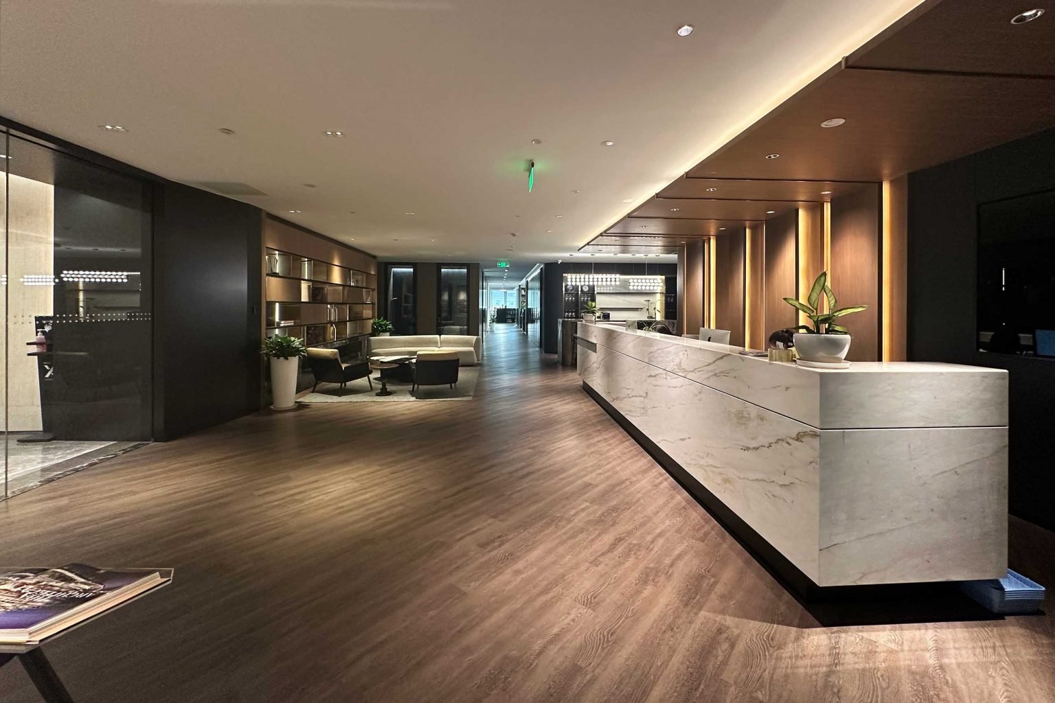 Sleek lobby with wooden floors, marble reception desk, modern lighting, and seating area with plants, creating a warm and inviting atmosphere.