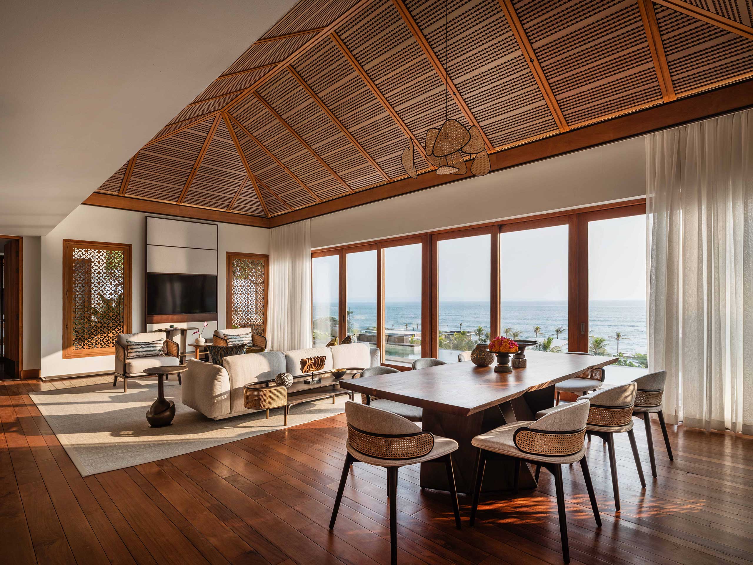 Luxurious open living space of a suite with a wooden ceiling, large windows showing a sea view. Features cozy furniture, elegant decor, and a serene ambiance.
