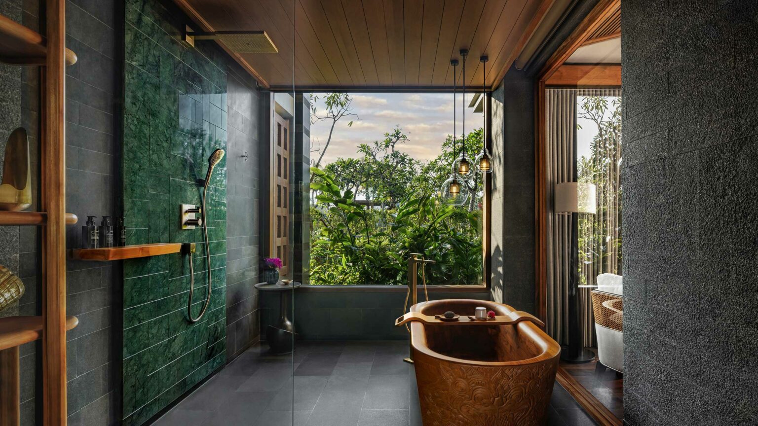 Luxurious suite bathroom with a wooden bathtub, large glass shower, and lush greenery outside a wide window. Warm lighting creates a cozy, serene ambiance.