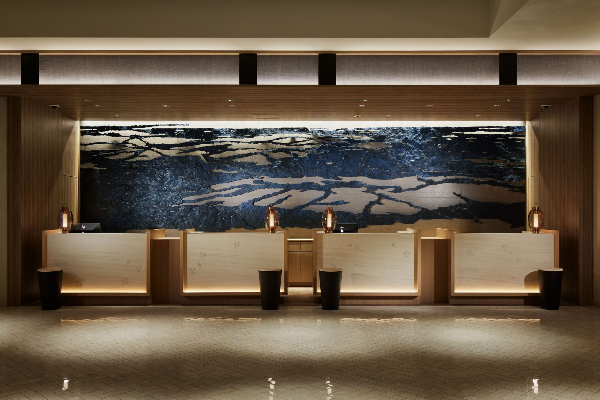 Modern hotel reception with sleek wooden desks, artistic wall art resembling dark waves, and soft, warm lighting creating a calm, welcoming atmosphere.