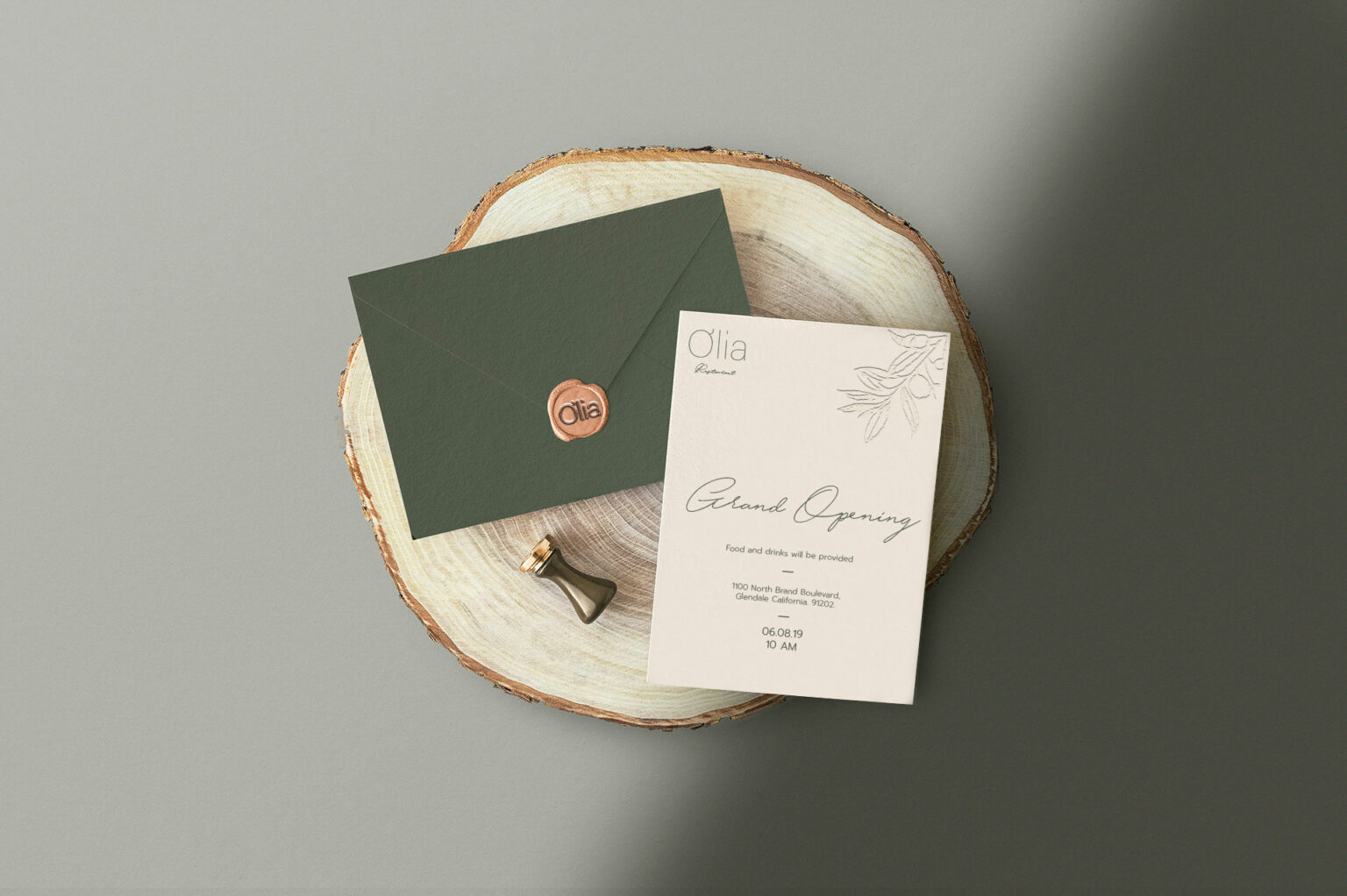 Olia Restaurant branding collaterals, featuring an invitation and dark green envelope with wax seal placed on a wooden slice. Invitation reads 