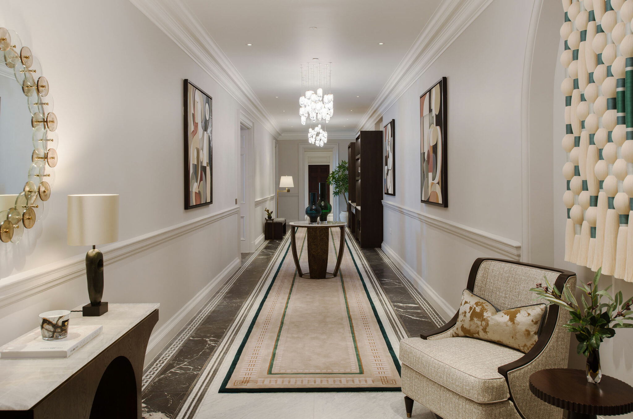Elegant hallway with modern art on white walls, a central console table, chandeliers, and sleek furniture. The tone is luxurious and sophisticated.