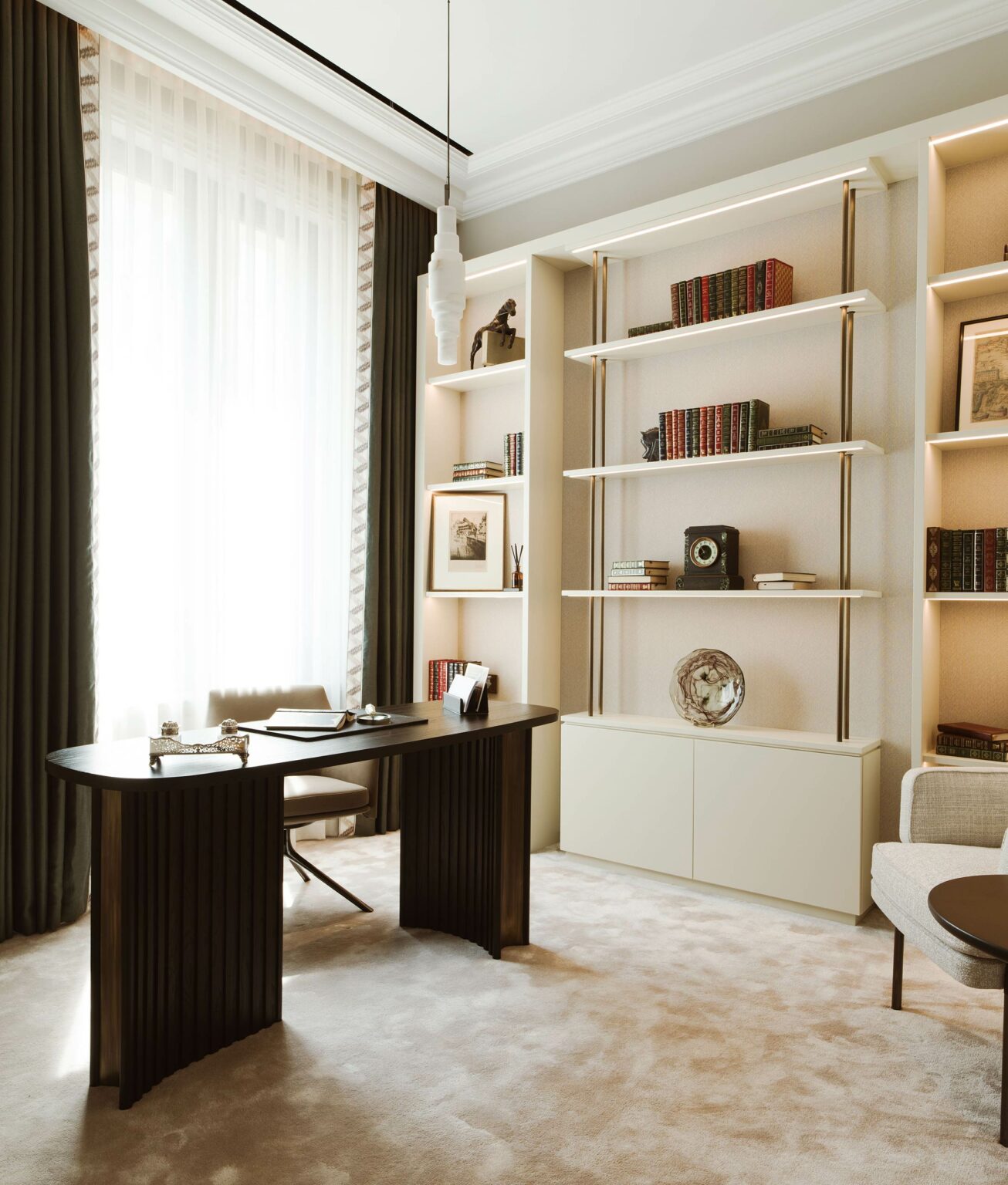 Modern study with a dark wood desk, chair, and open shelves filled with books and decor, set against a sunlit window with sheer curtains.