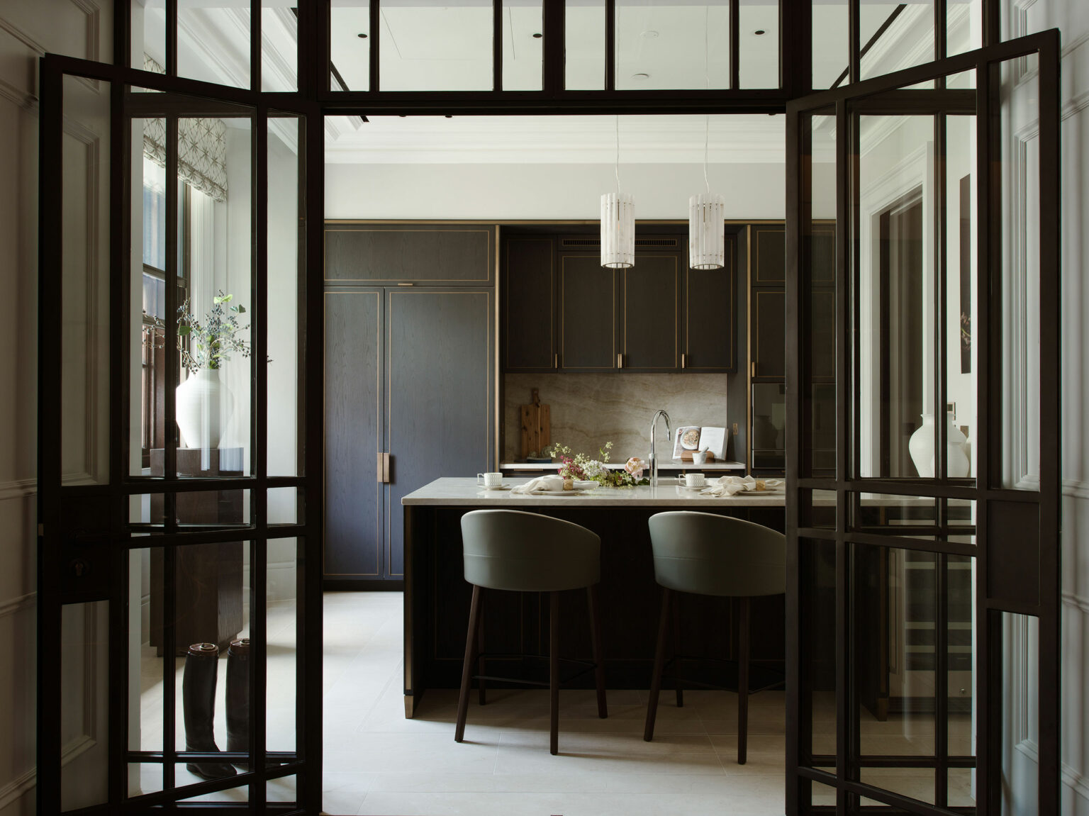 Modern kitchen with dark wood cabinets, a central island with two gray chairs, and pendant lights. A vase with flowers adds a fresh touch.