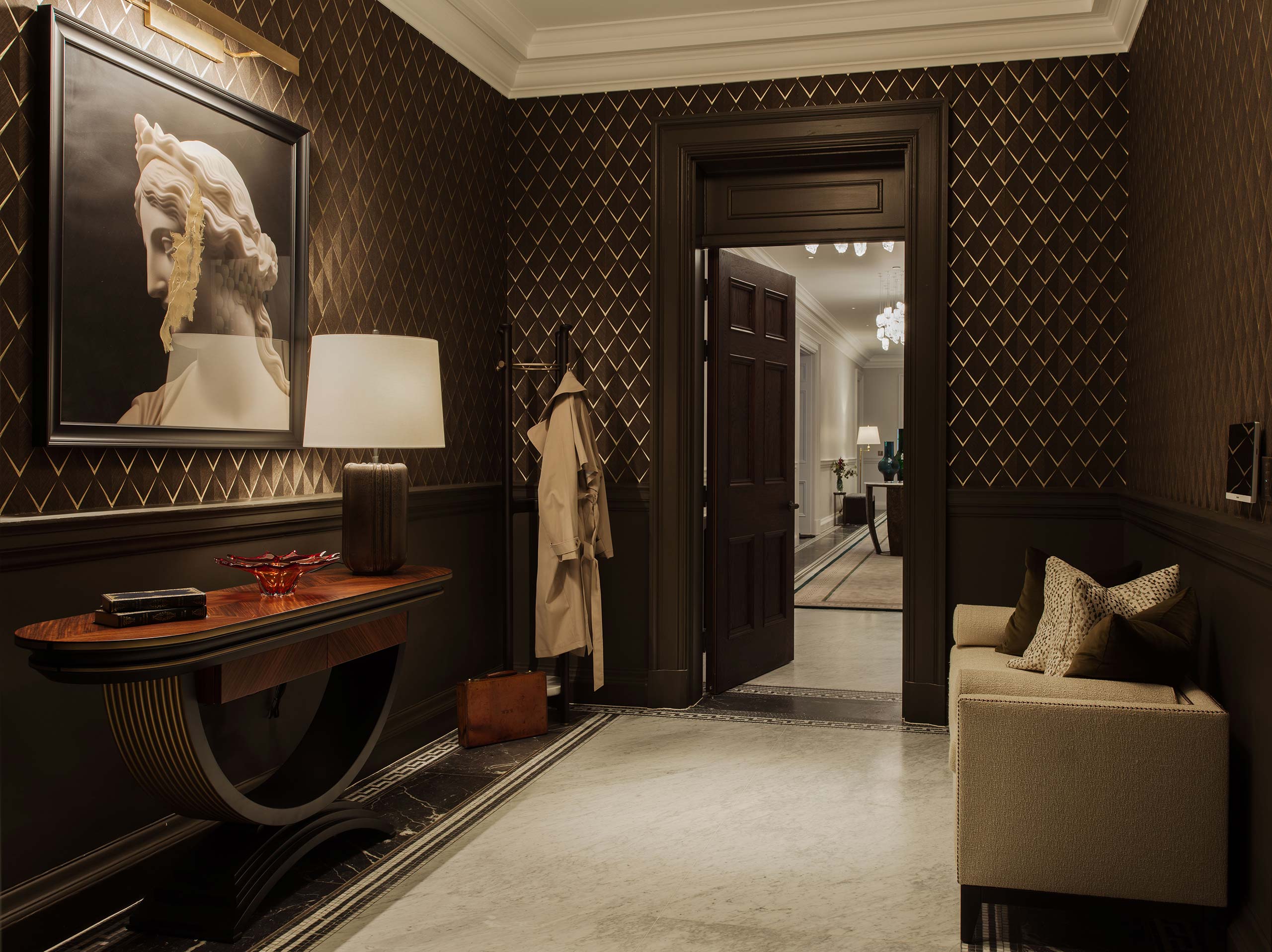 A luxurious hallway with dark diamond-patterned walls features a classical bust painting, elegant side table, and cozy sofa, conveying a warm, refined ambiance.