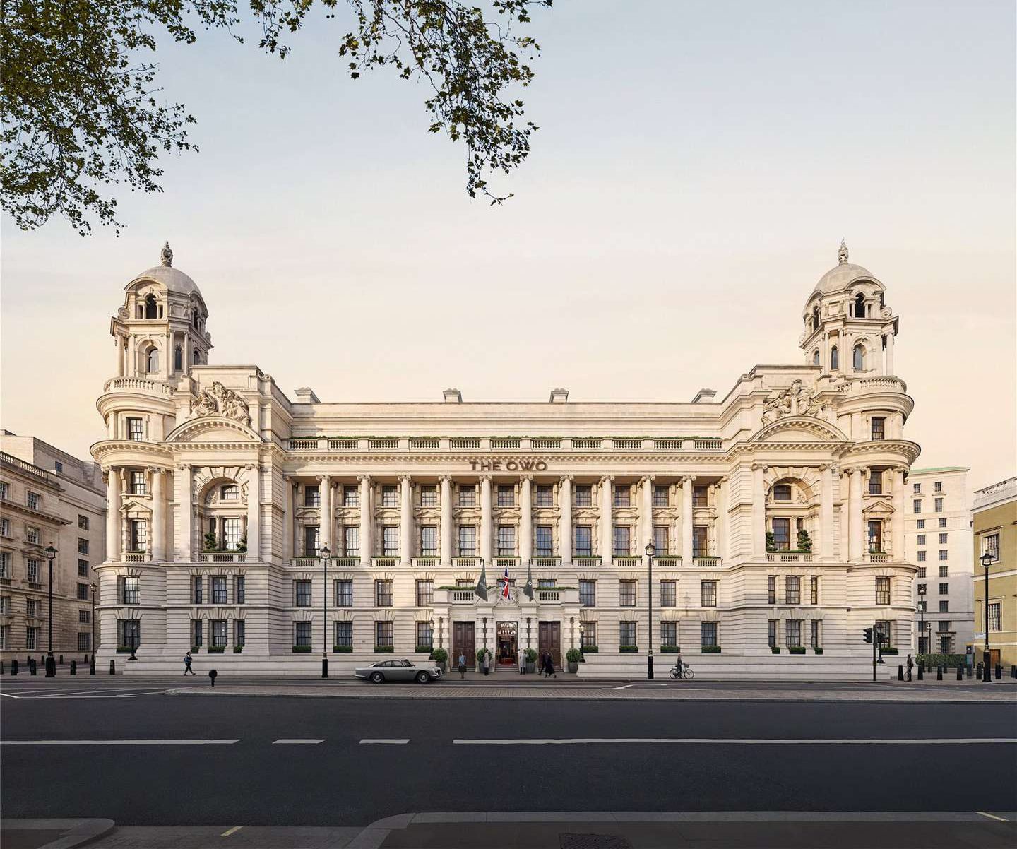 The OWO Residences by Raffles exteriors. Majestic neoclassical building with grand columns, ornate facades, and two towers; the setting is serene with a pale sky and sparse traffic.