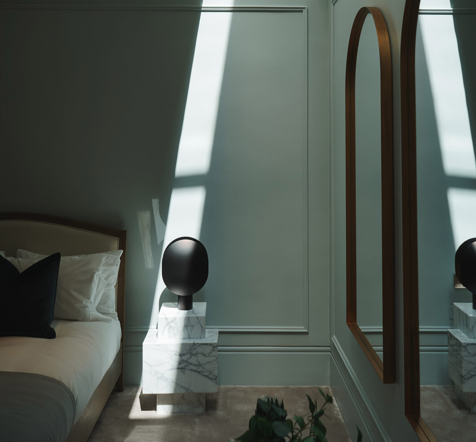 Minimalist bedroom with soft green walls, sunlight streaming in. A modern black lamp on a marble stand casts shadows. Calm and serene mood.