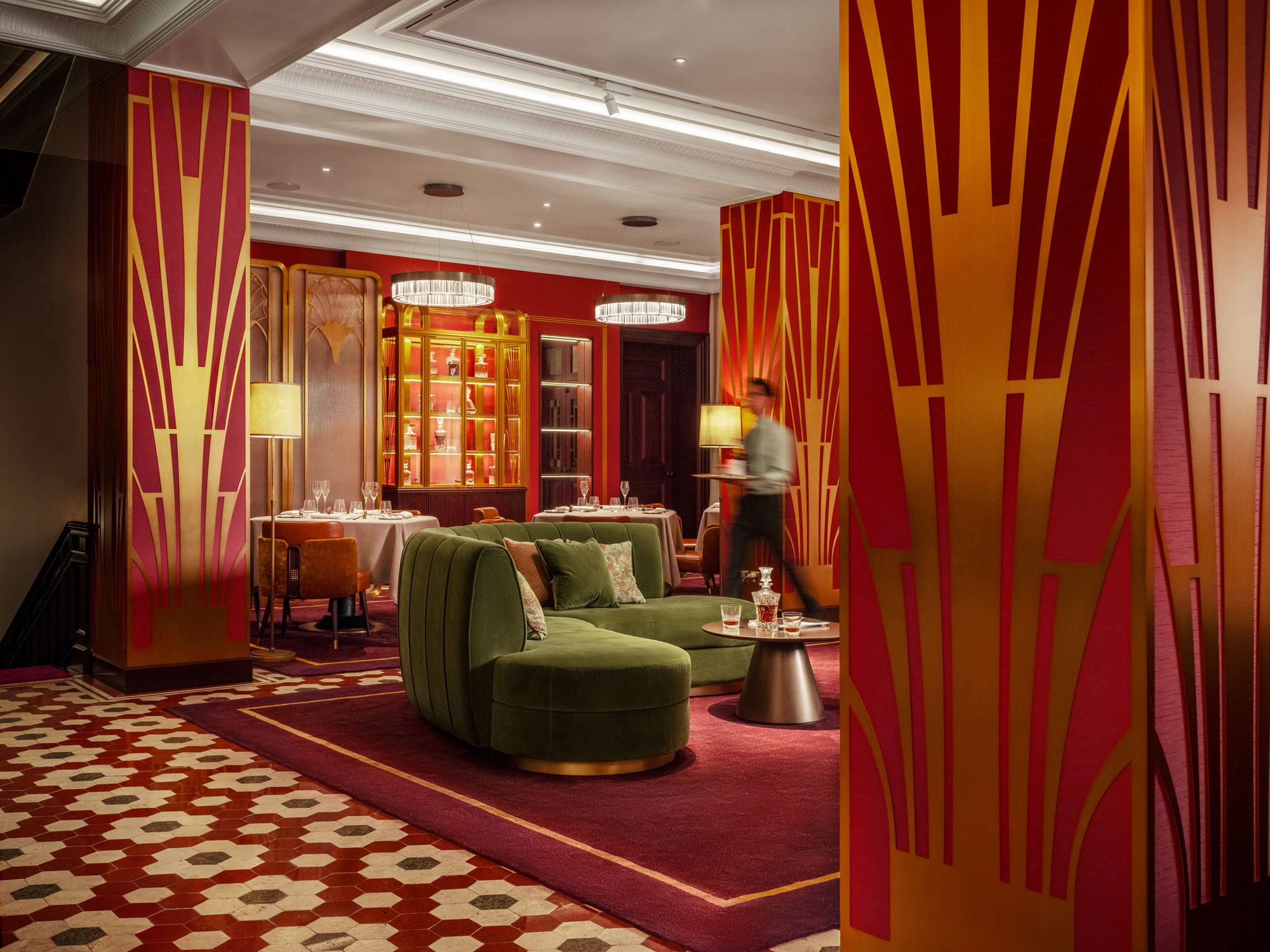 Art deco-inspired private club lounge with rich red and gold walls, green velvet sofas, and geometric patterns. Elegant ambiance with warm lighting and artful decor.