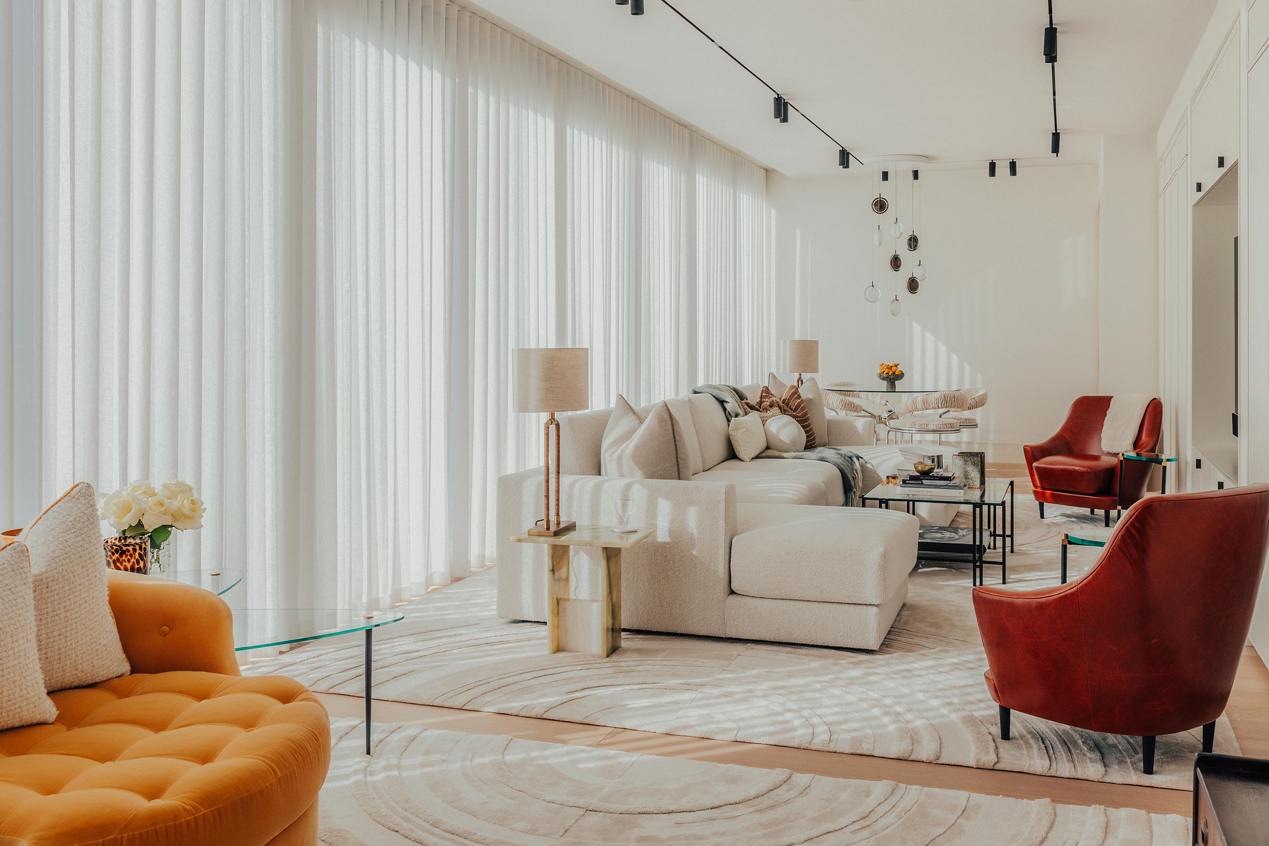 Modern living room with cozy beige sofas, vibrant orange and red chairs, and sheer curtains. Soft lighting and elegant décor create a warm, inviting atmosphere.