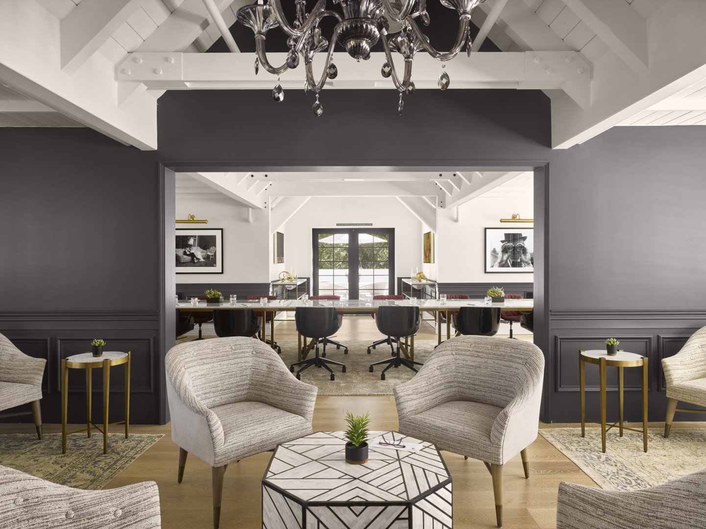 Stylish hotel meeting space with modern chairs, geometric coffee table, and a chandelier. Neutral tones and art create an elegant, inviting atmosphere.