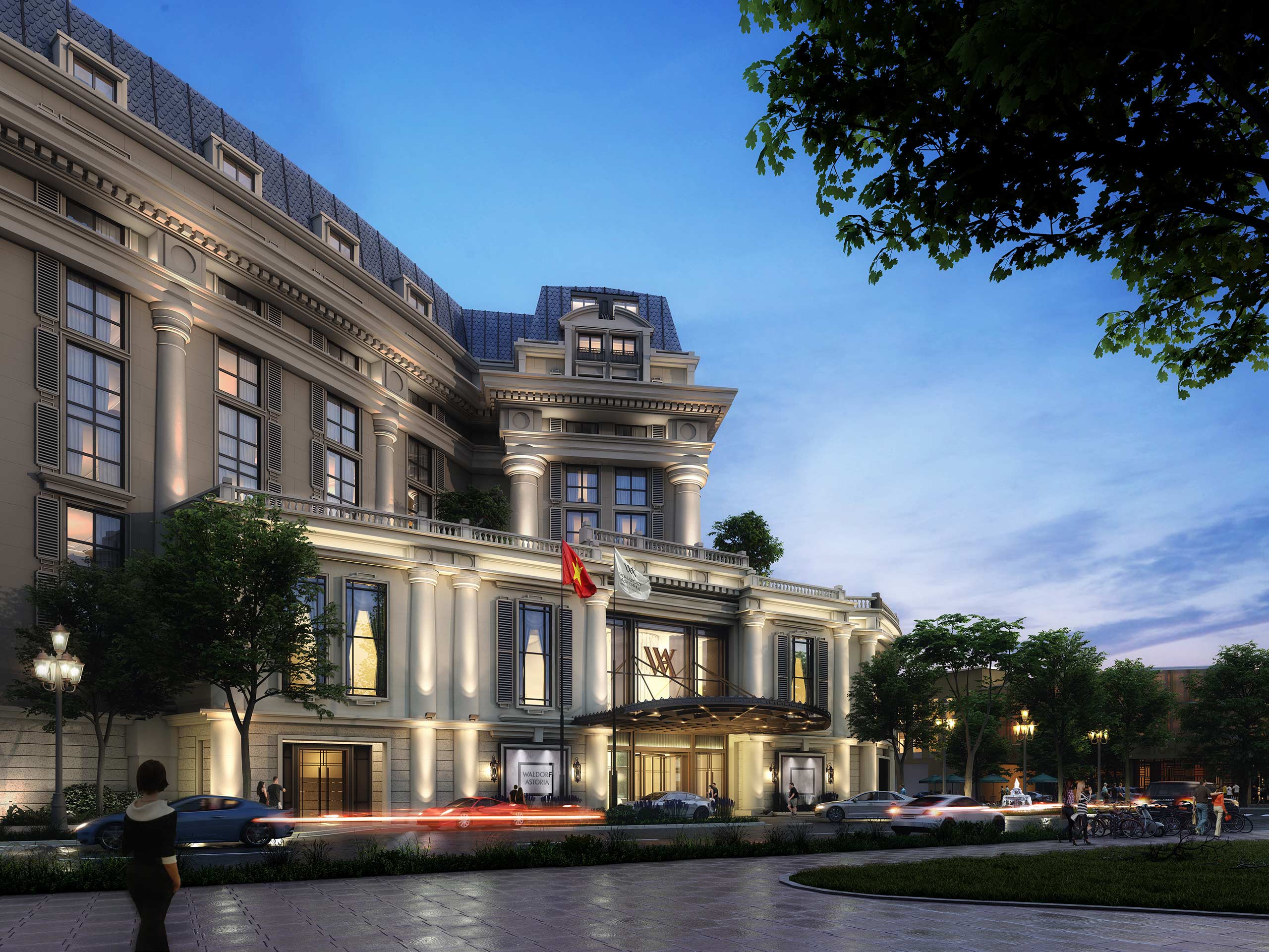 Exterior of Waldorf Hanoi Opera Hotel, Vietnam, featuring an elegant, illuminated building with classical columns and mansard roof at dusk. Flags and trees add grandeur, while cars pass by on a bustling street.