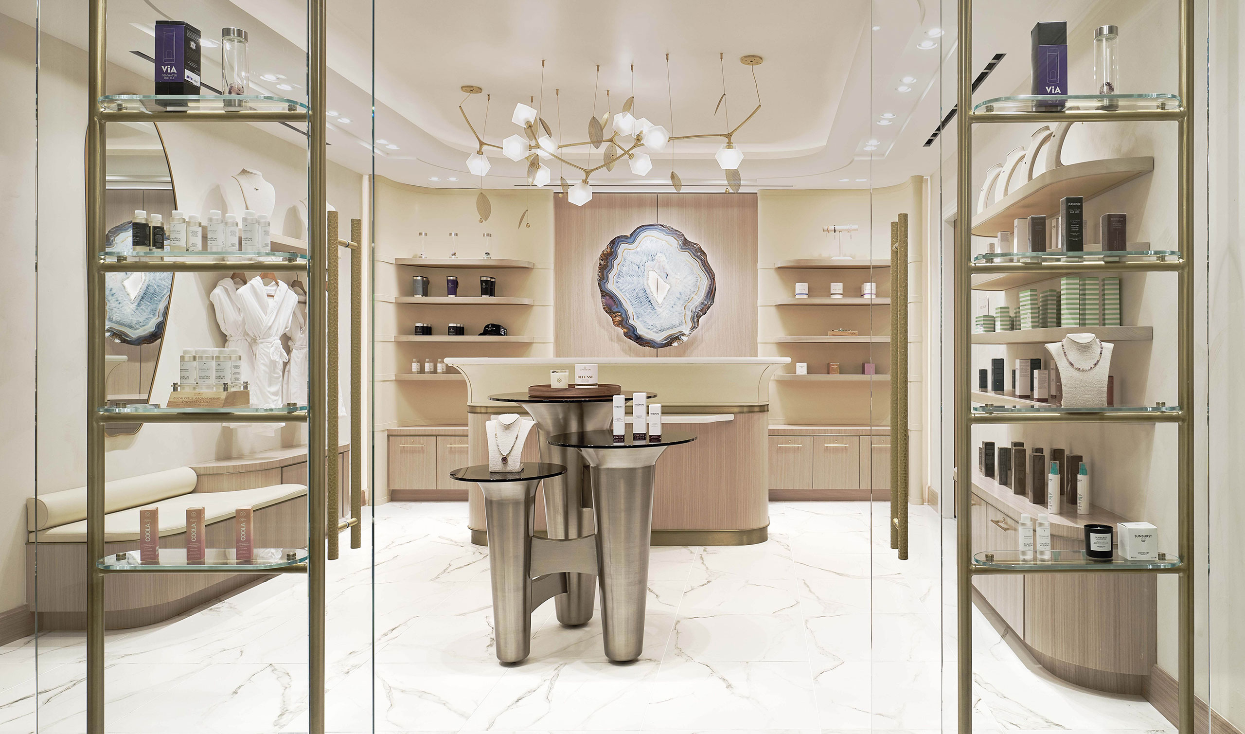 Luxurious hotel spa arrival with a decorative geode wall art, sleek product displays on modern black tables, warm lighting, and elegant shelving.