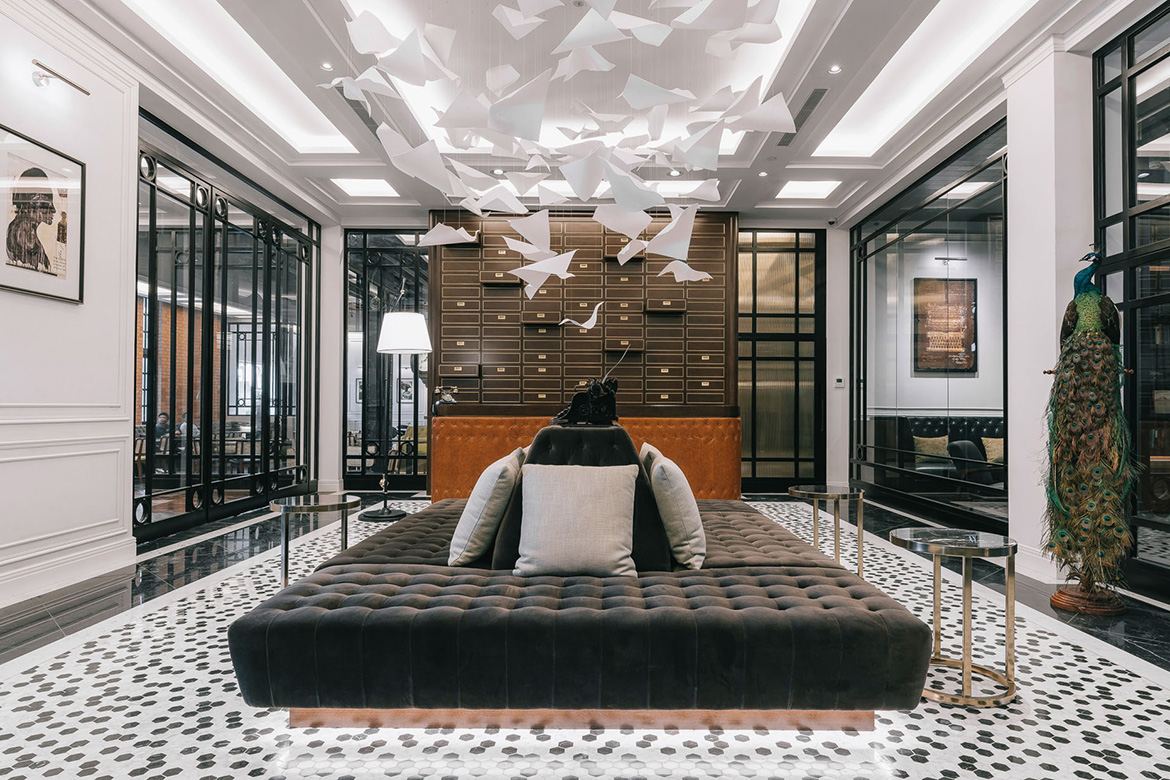 Luxurious hotel lobby with elegant decor. Features a plush, dark tufted sofa, geometric ceiling art, and a colorful peacock sculpture. Sophisticated ambiance.
