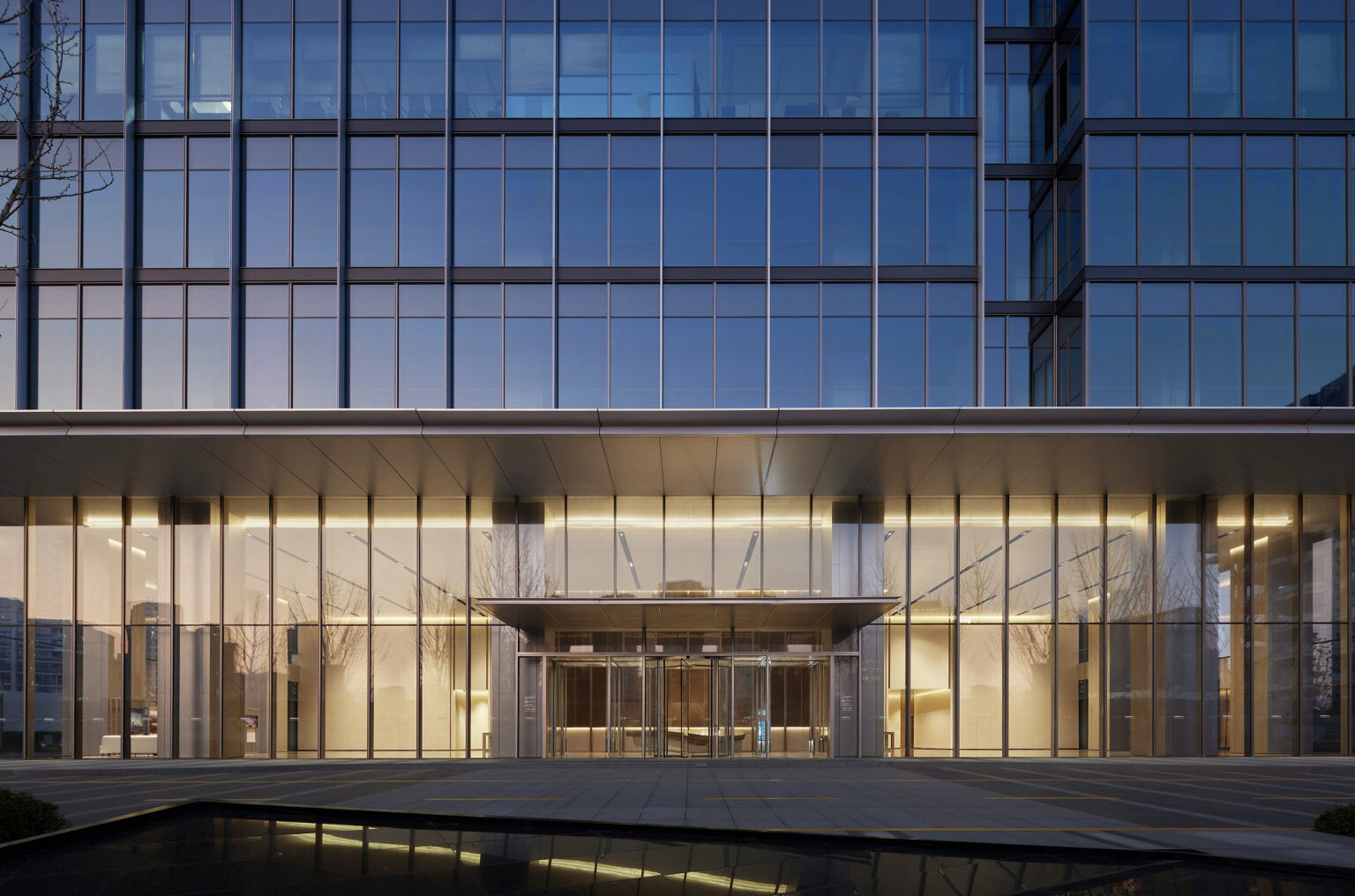 Sleek modern hotel building entrance with large glass doors, reflecting a calm, twilight sky. The structure conveys a sense of sophistication and elegance.