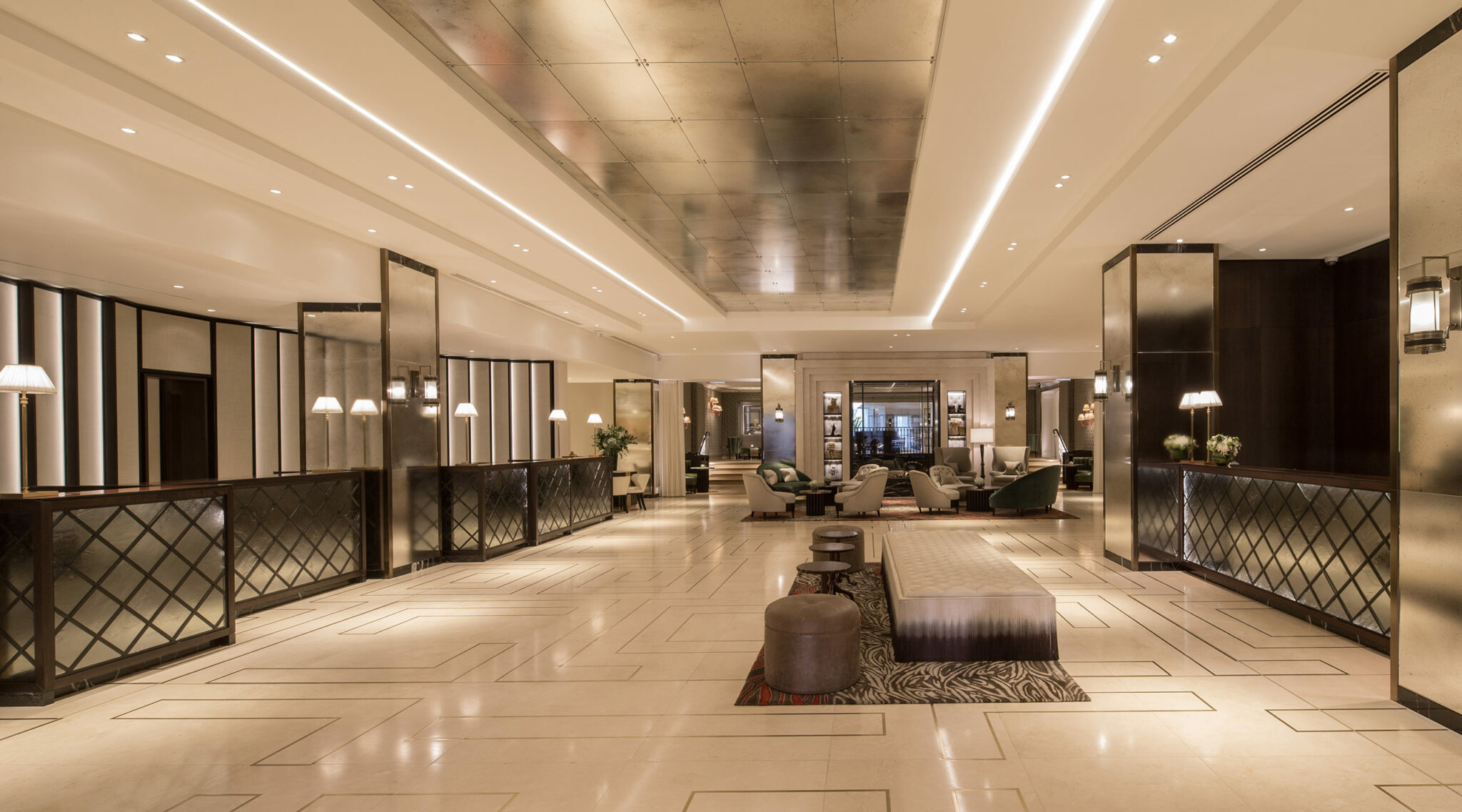 Luxurious hotel lobby with elegant lighting, mirrored panels, and plush seating. Sleek decor and neutral tones convey a sophisticated ambiance.