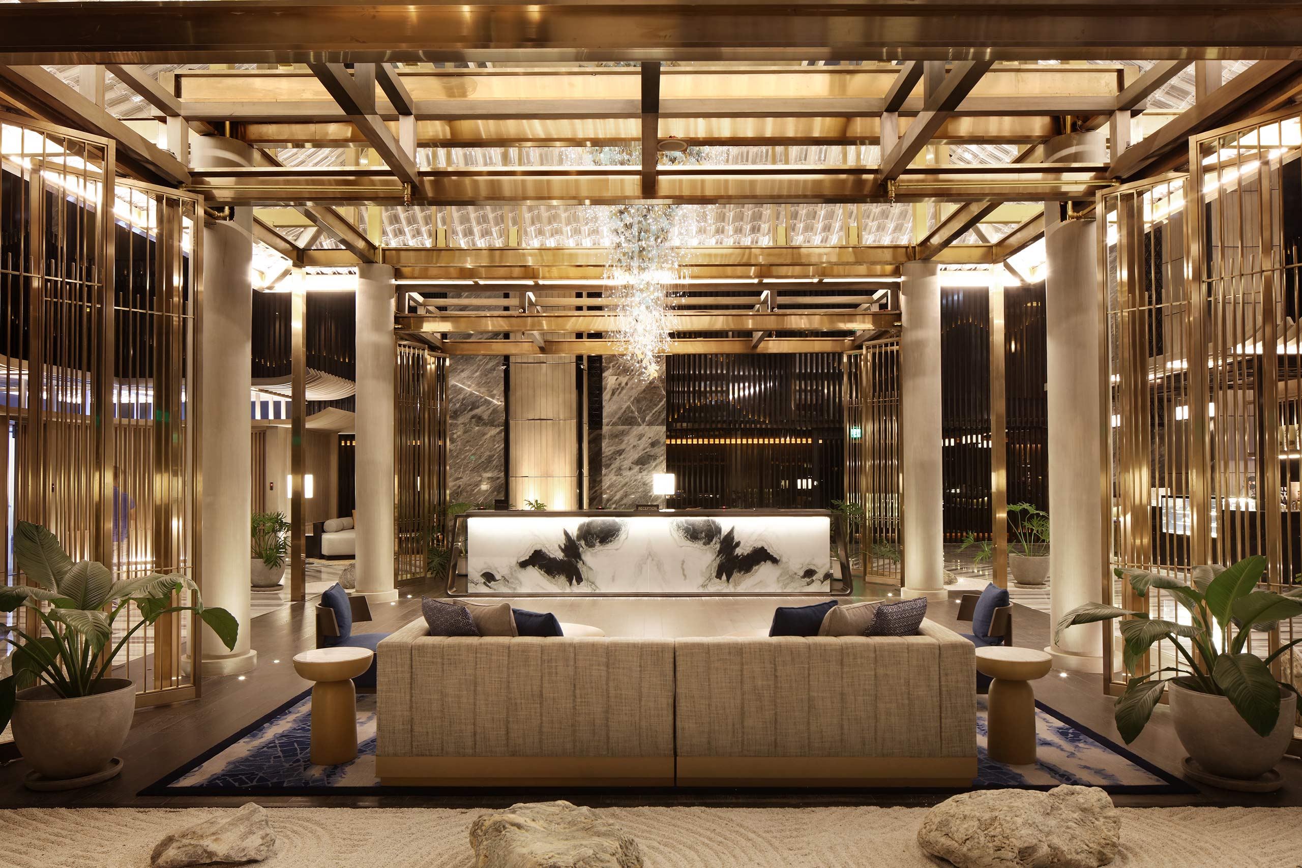 Luxurious hotel lobby with a marble front desk, elegant chandelier, plush seating, and gold accents. Warm, inviting atmosphere with a modern design.