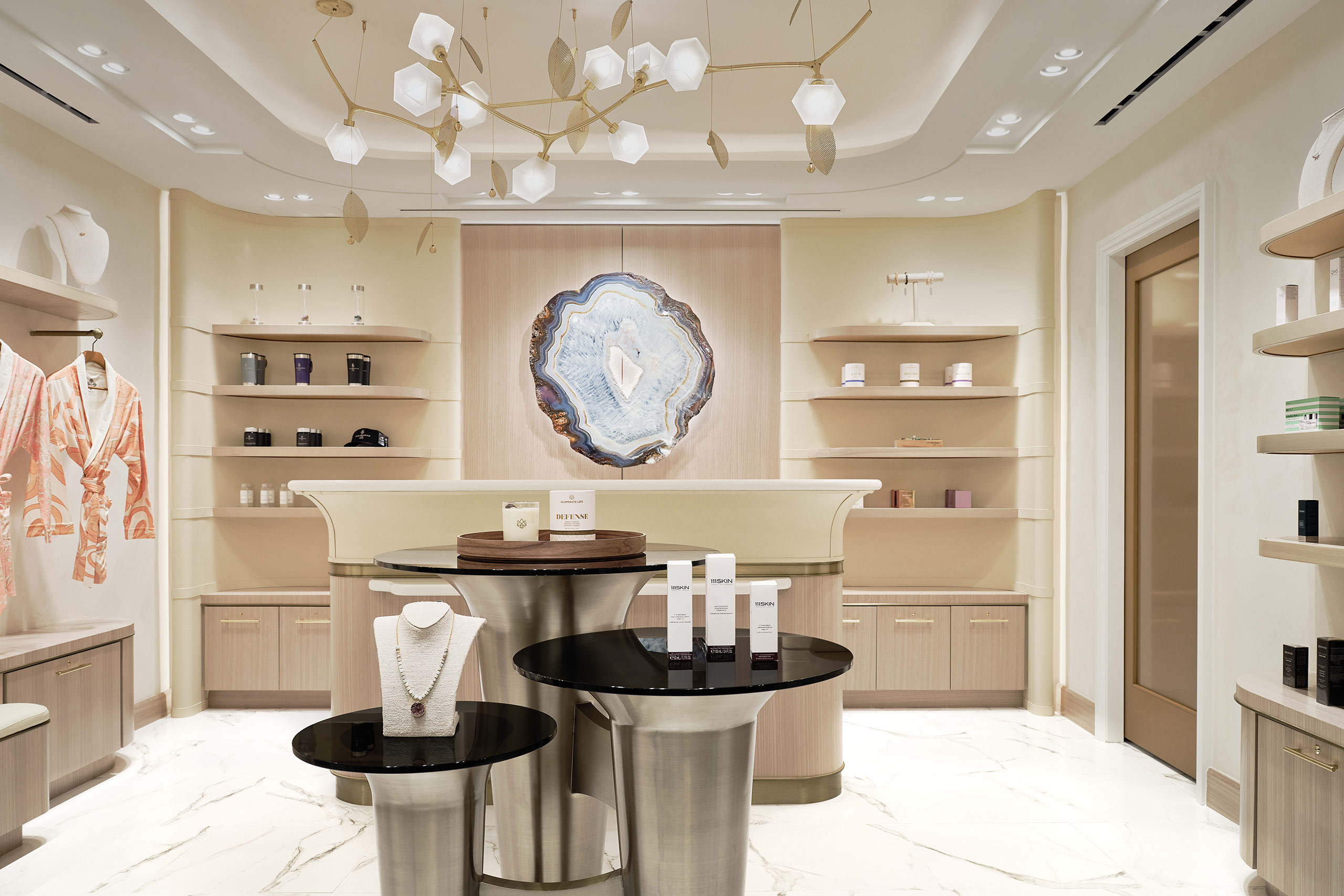 Luxurious hotel spa arrival with a decorative geode wall art, sleek product displays on modern black tables, warm lighting, and elegant shelving.