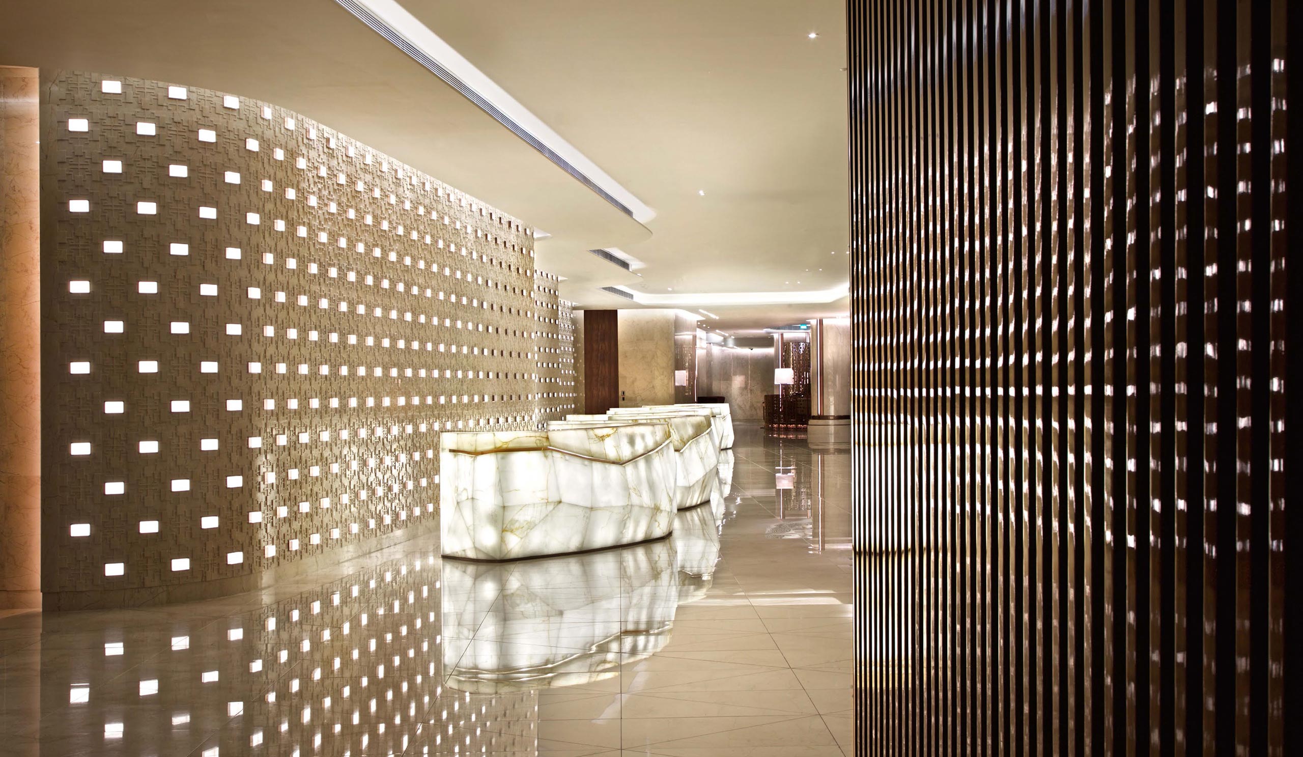 Luxurious hotel lobby with glowing marble check-in counters and a textured, illuminated wall creating a modern and elegant atmosphere.