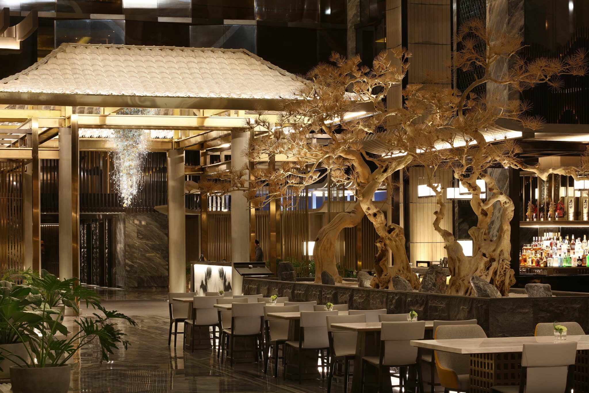 Luxurious hotel all day dining featuring elegant wooden sculptures, white-roofed pavilion, marble floors, stylish seating, and a chic bar, creating a sophisticated ambiance.