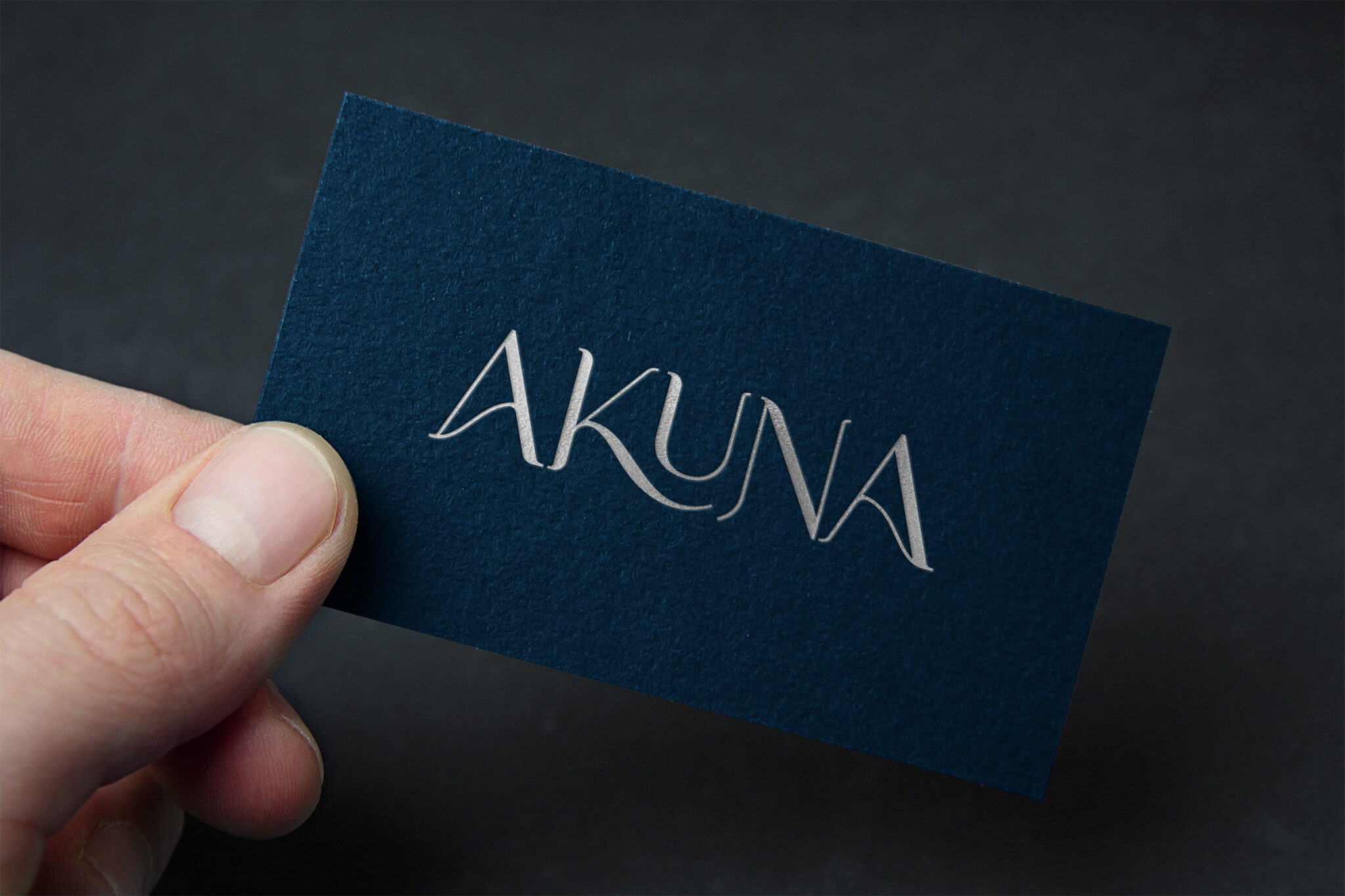 A hand holds a dark blue business card with the word 