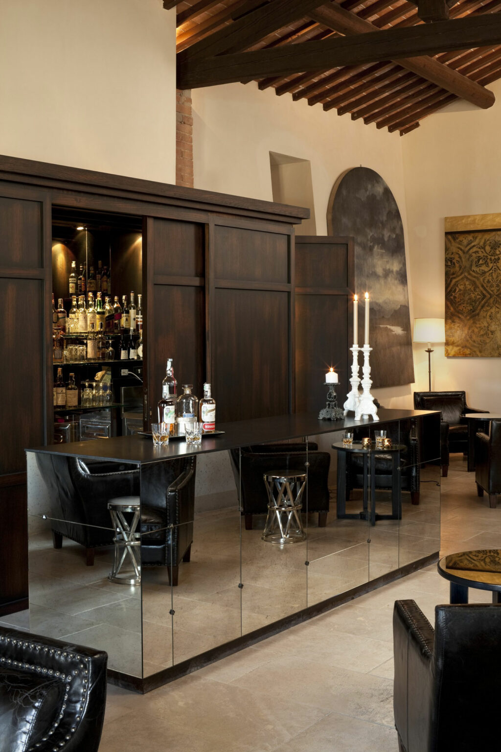 Luxurious hotel bar setting with dark wood paneling, mirrored surfaces, and leather chairs. Bottles and candles create an elegant, cozy ambiance.