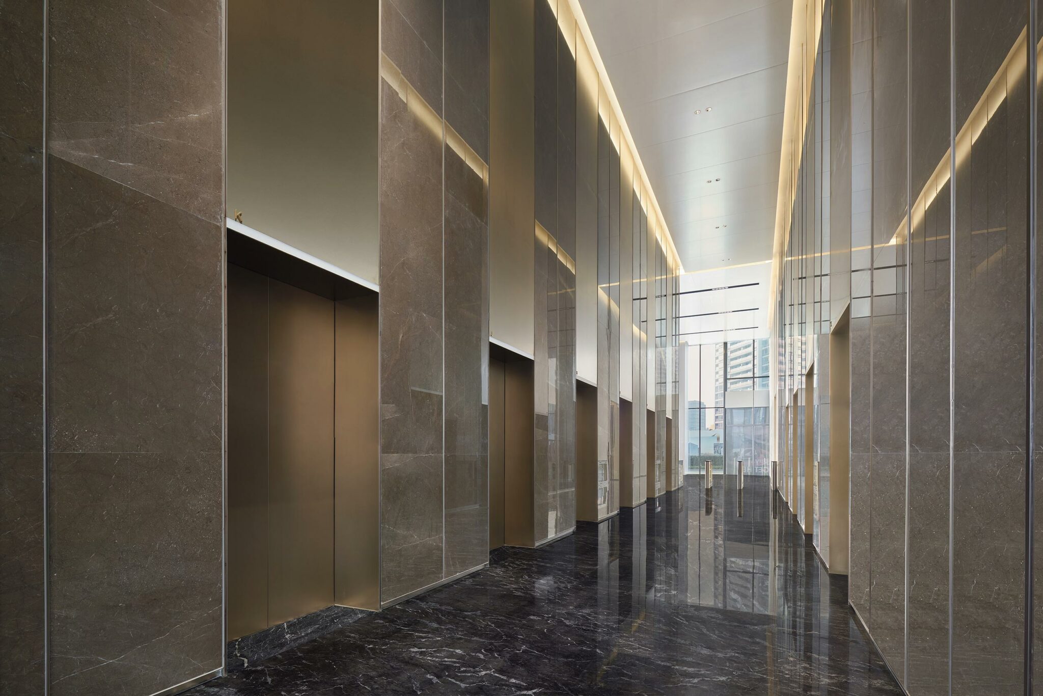 Modern office building lift lobby with tall, reflective marble walls and sleek elevator doors. Bright lighting and a polished floor create an upscale, elegant ambiance.