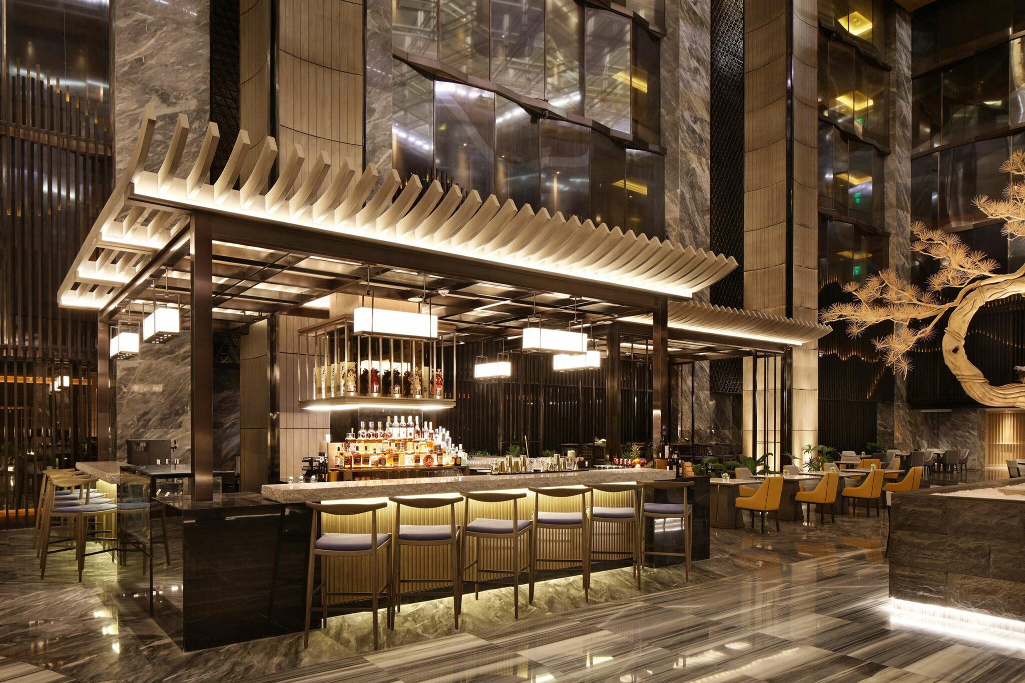 Luxurious hotel bar with a modern design, featuring a stylish, illuminated canopy and marble accents. Rows of bottles and plush seating create an elegant ambiance.