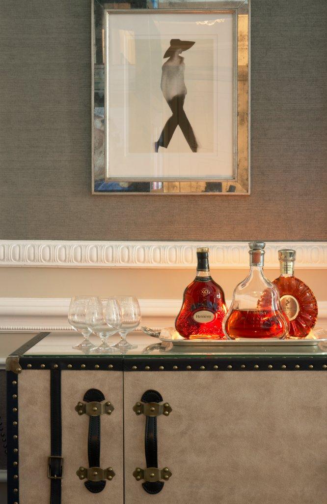 Chic suite living interior with framed silhouette art above liquor bottles and glasses on a cabinet. Elegant, refined ambiance with a touch of luxury.