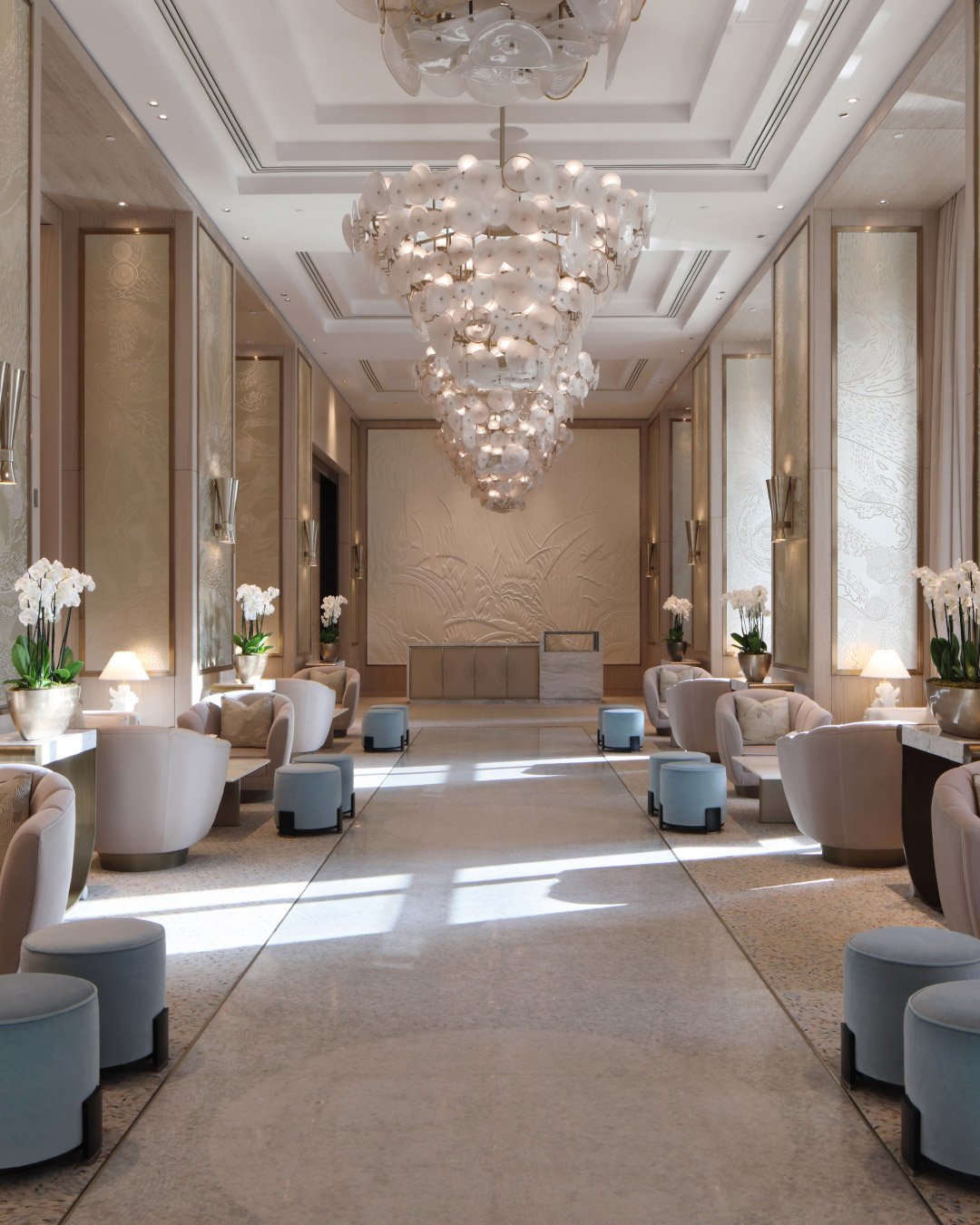 Luxurious hotel lobby with ornate, cascading chandelier and soft lighting. Elegant armchairs line the walls, creating a welcoming, sophisticated atmosphere.