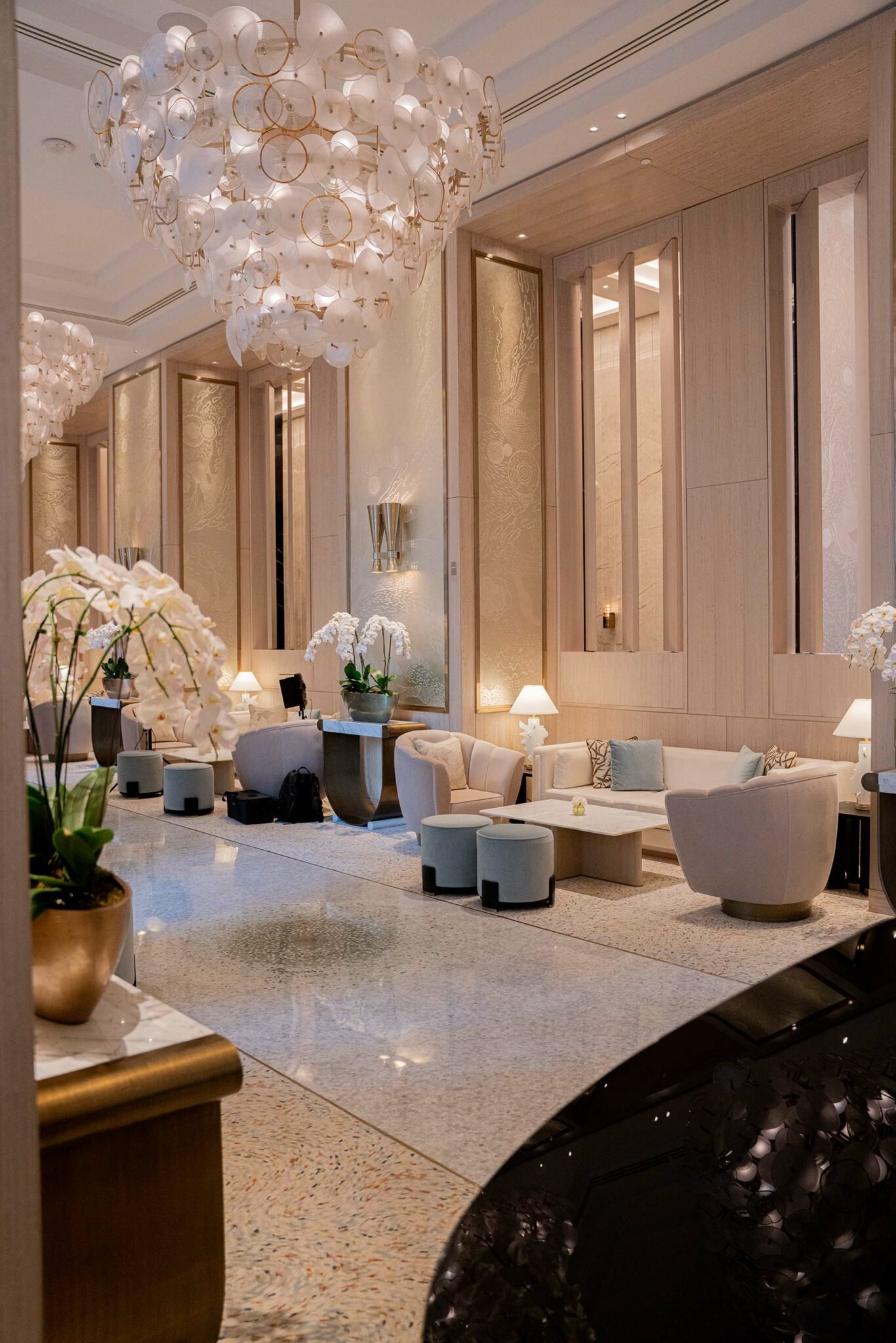 Luxurious hotel lobby with elegant chandeliers, cream-colored sofas, and plush chairs. Orchids and soft lighting create a serene, upscale ambiance.