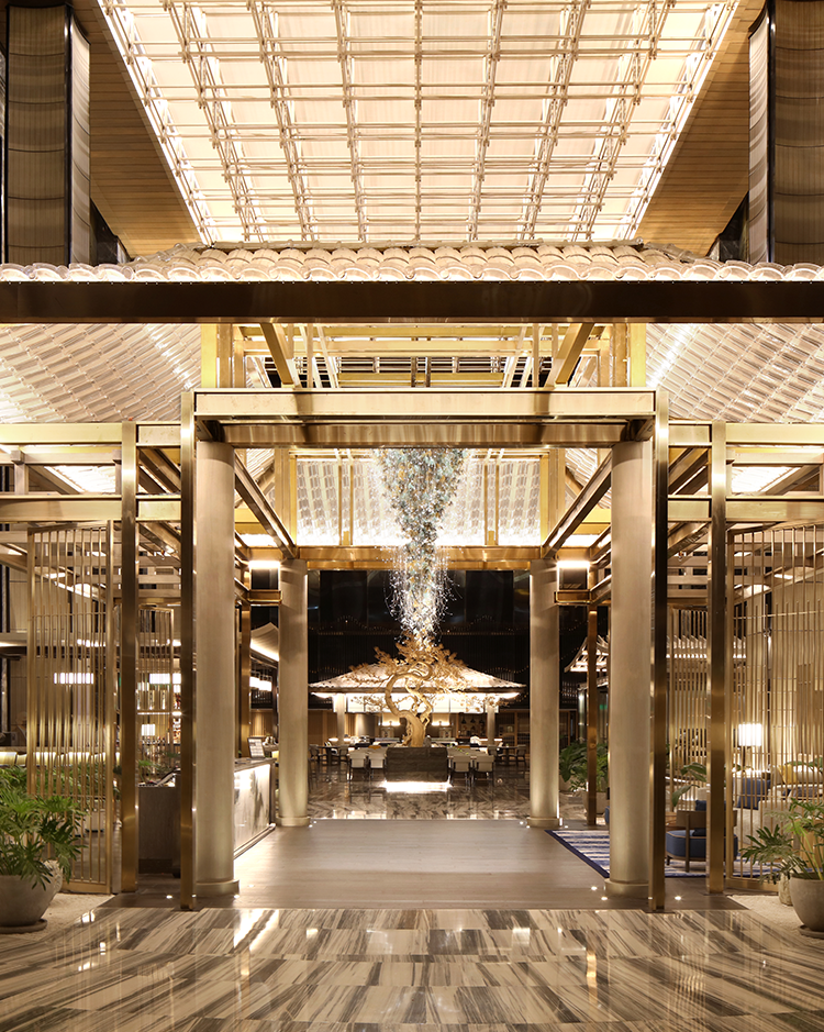 Luxurious hotel lobby featuring a grand golden portal, sculptural chandelier, statement tree installation, and integrated lighting under a vaulted glass ceiling.