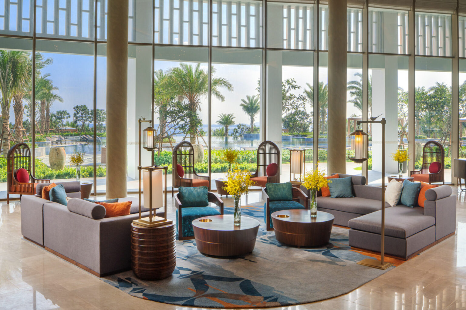 Modern hotel lobby with large windows overlooking a lush garden and pond. Cozy seating, vibrant cushions, and warm lighting create an inviting atmosphere.