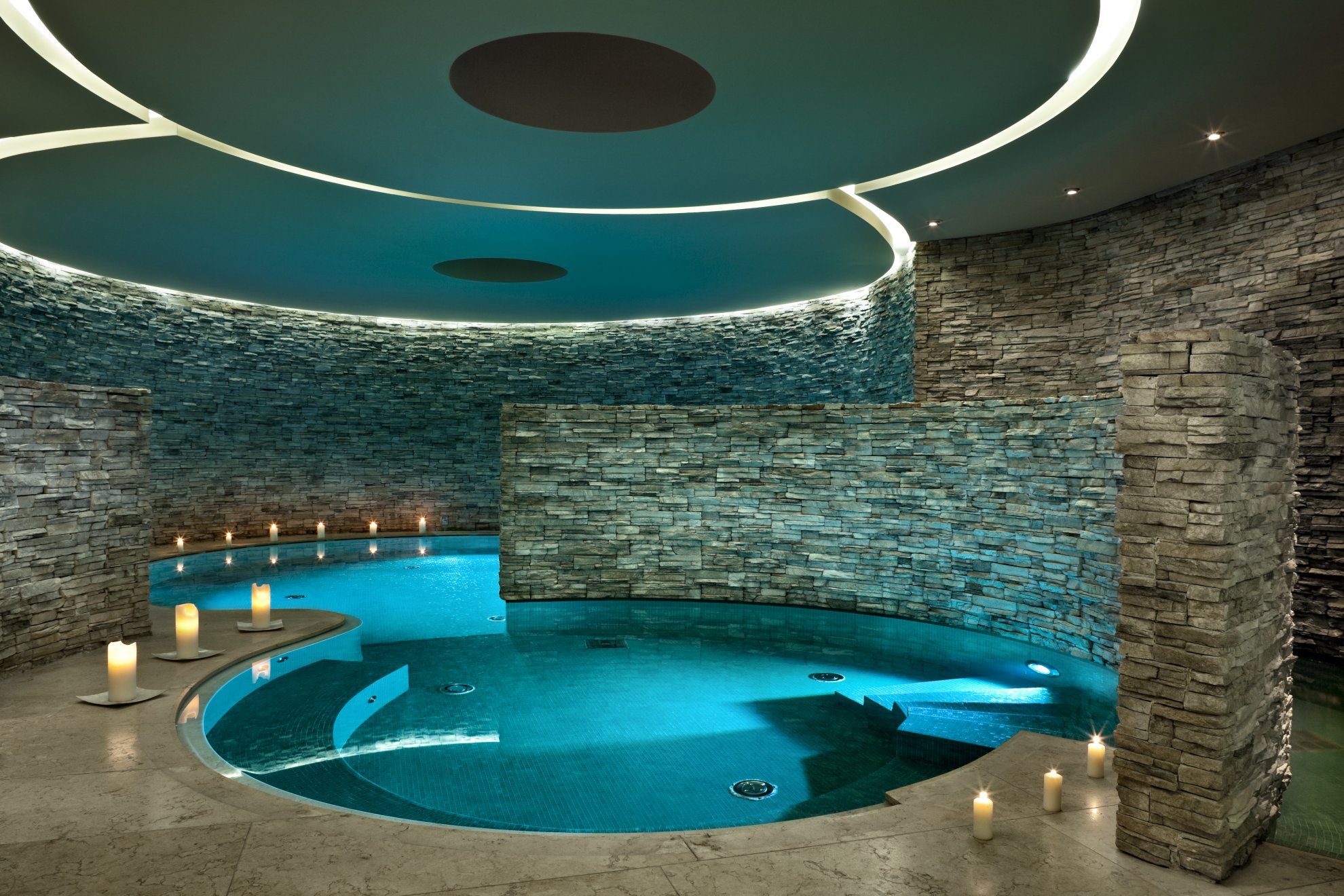 Elegant indoor pool with stone walls, ambient lighting, and glowing candles. The tranquil setting conveys a calm, spa-like atmosphere.