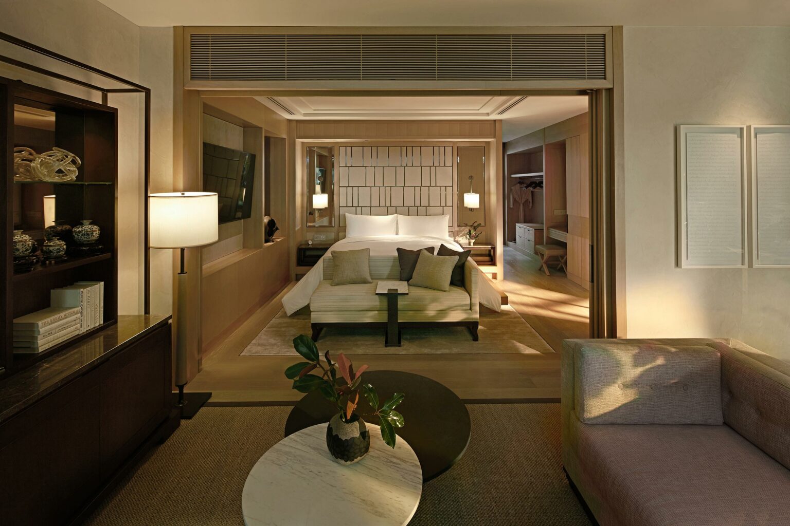 Stylish hotel room with a cozy bed, modern decor, and warm lighting. A plush sofa and decorative plants create an inviting, luxurious atmosphere.