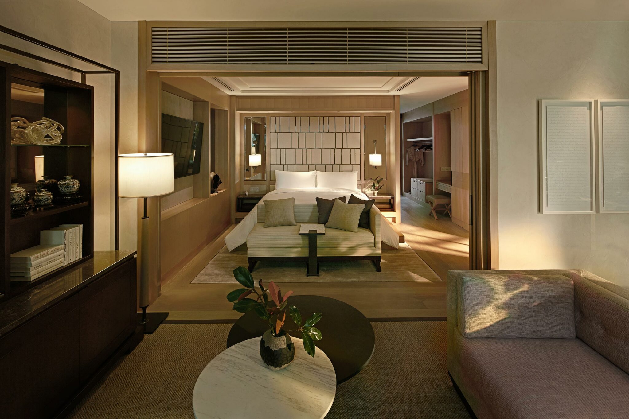 Stylish hotel room with a cozy bed, modern decor, and warm lighting. A plush sofa and decorative plants create an inviting, luxurious atmosphere.