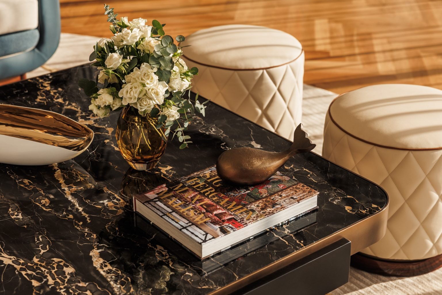 Elegant suite living room with a geometric-patterned cabinet, a round table surrounded by plush chairs, a central floral arrangement, and a modern chandelier.