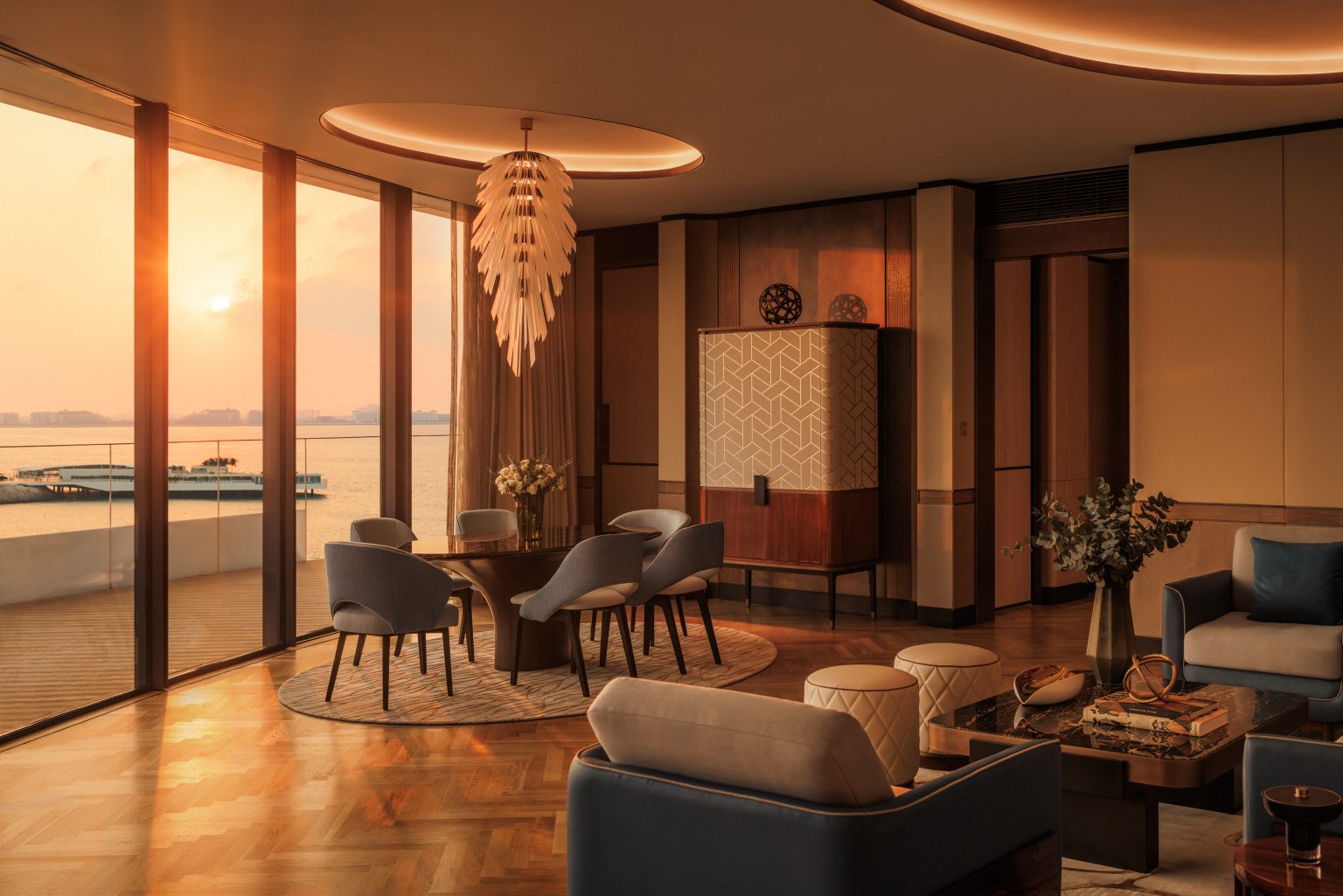 Elegant suite living room with a geometric-patterned cabinet, a round table surrounded by plush chairs, a central floral arrangement, and a modern chandelier.