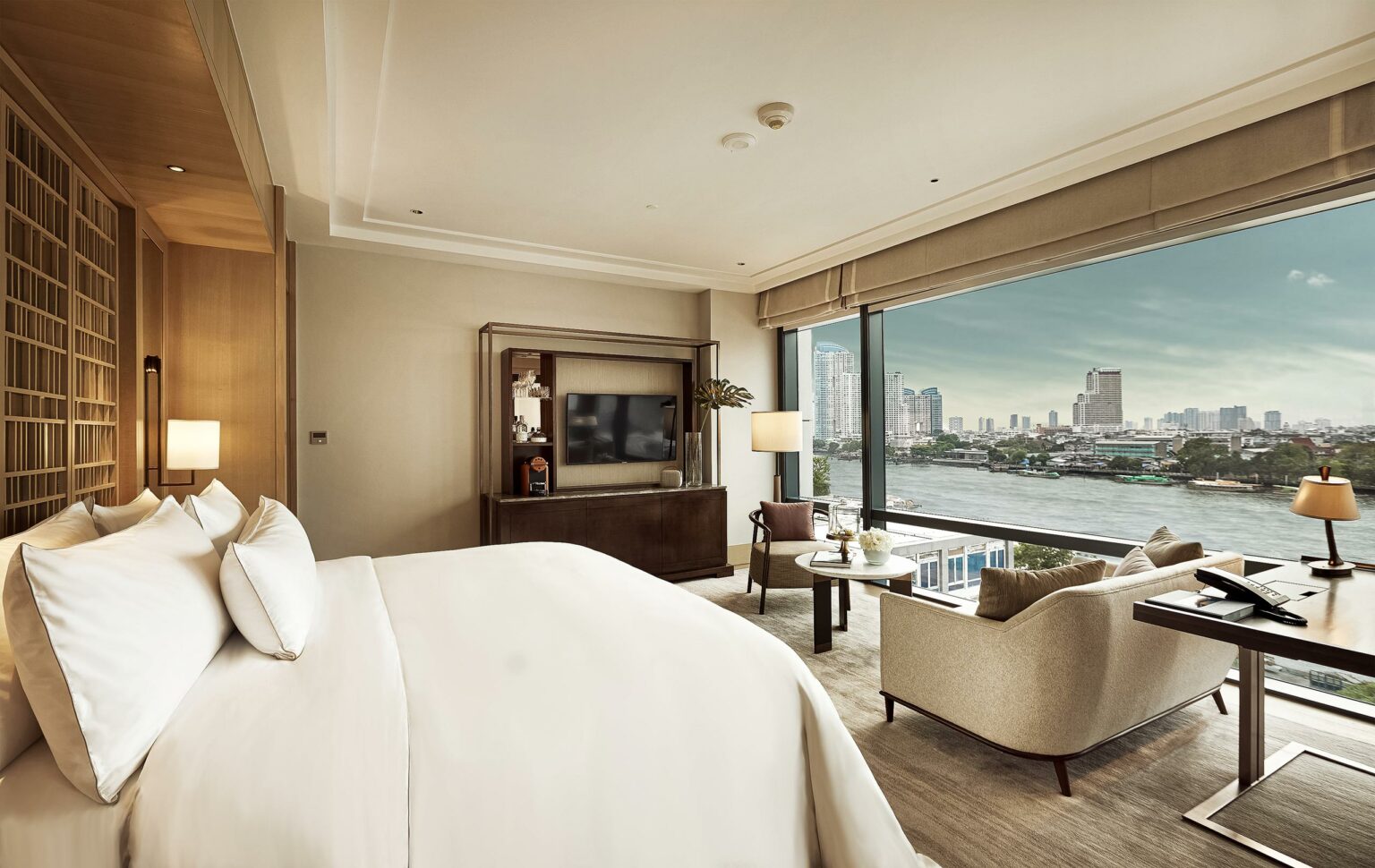 Luxurious hotel room with a white bed and large windows showcasing Bangkok's skyline. Soft lighting, elegant furniture, and a serene ambiance.