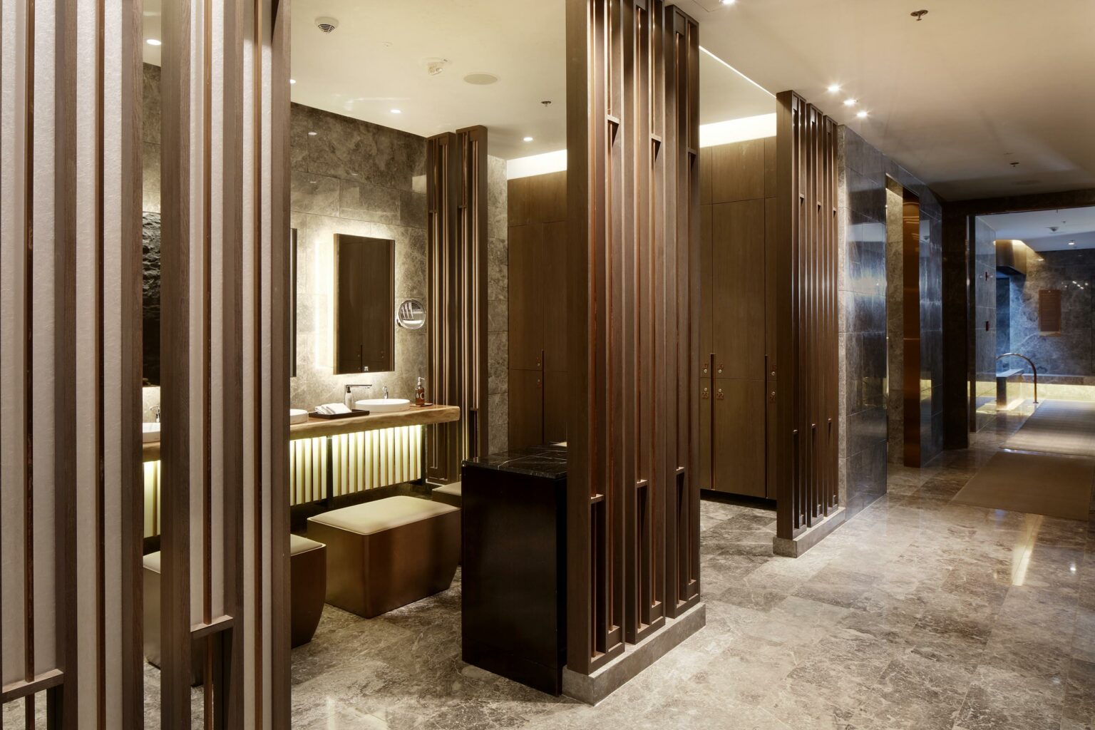 Luxurious hotel changing room with marble walls, wooden accents, and warm lighting. Features a modern sink, mirror, and sleek seating, conveying elegance.
