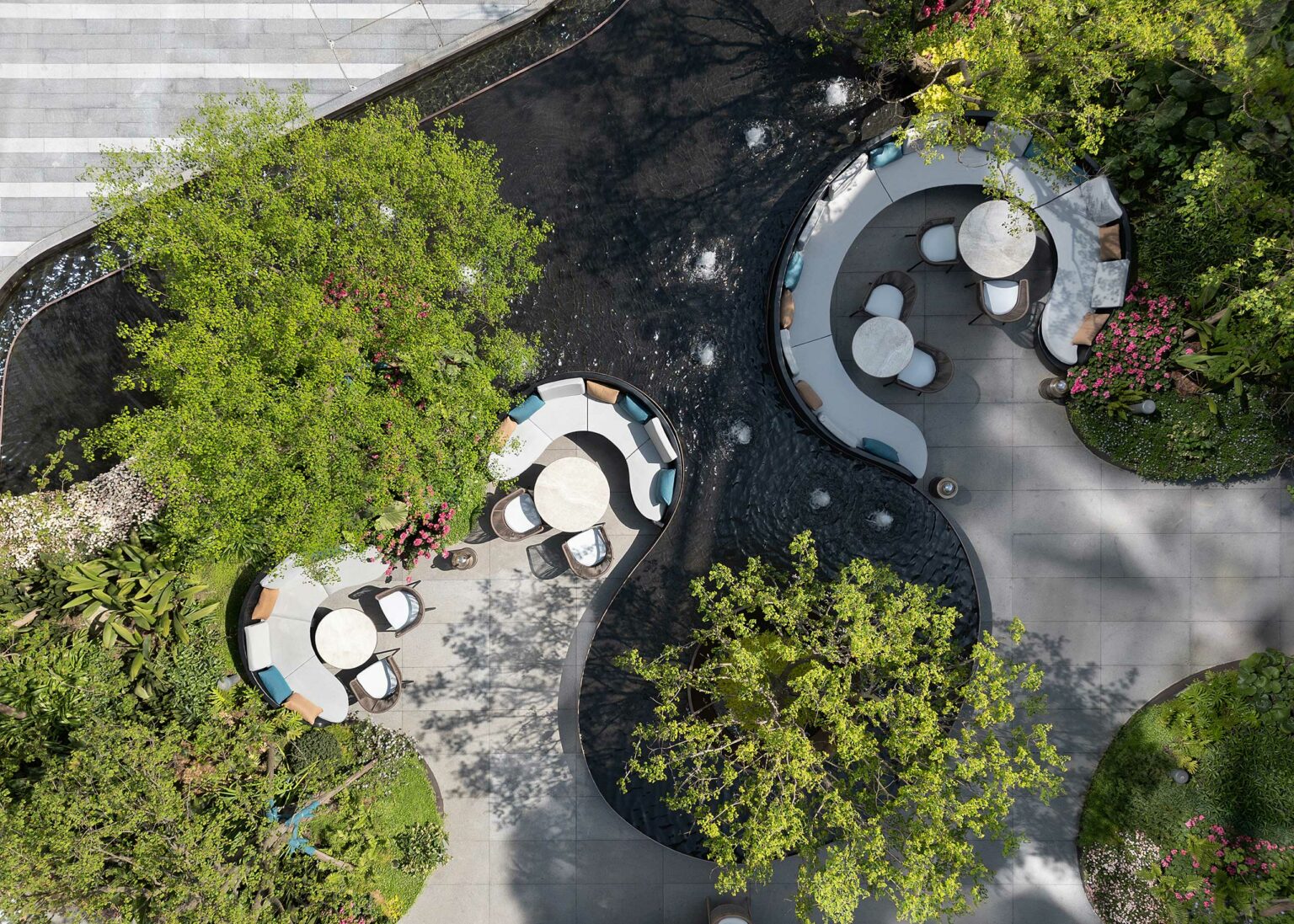 Aerial view of a serene commercial patio featuring yin-yang shaped seating areas surrounded by lush trees and a reflective black water feature, exuding tranquility.