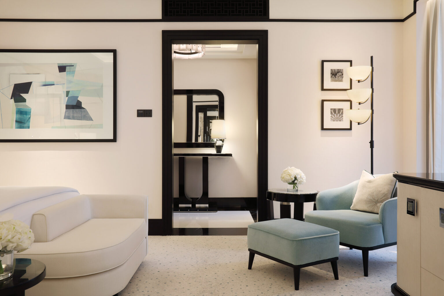 Elegant suite living room featuring a cream sofa, blue armchair with ottoman, abstract artwork, and a stylish lamp. The mood is modern and serene.
