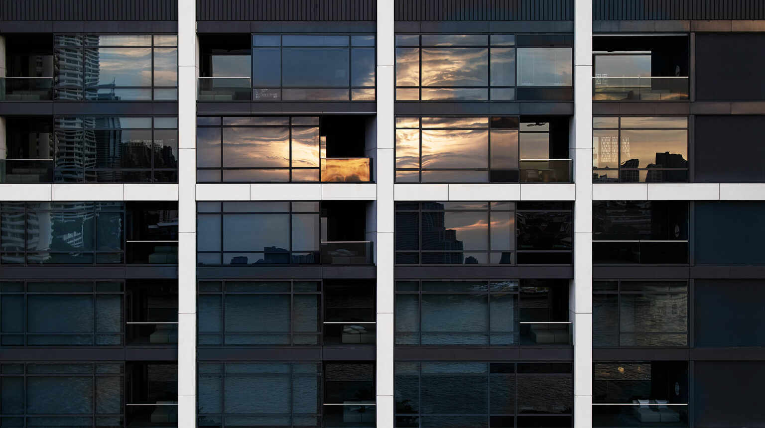 Reflection of a vibrant sunset with orange and pink hues on a modern hotel building's glass façade, creating a serene and tranquil urban scene.