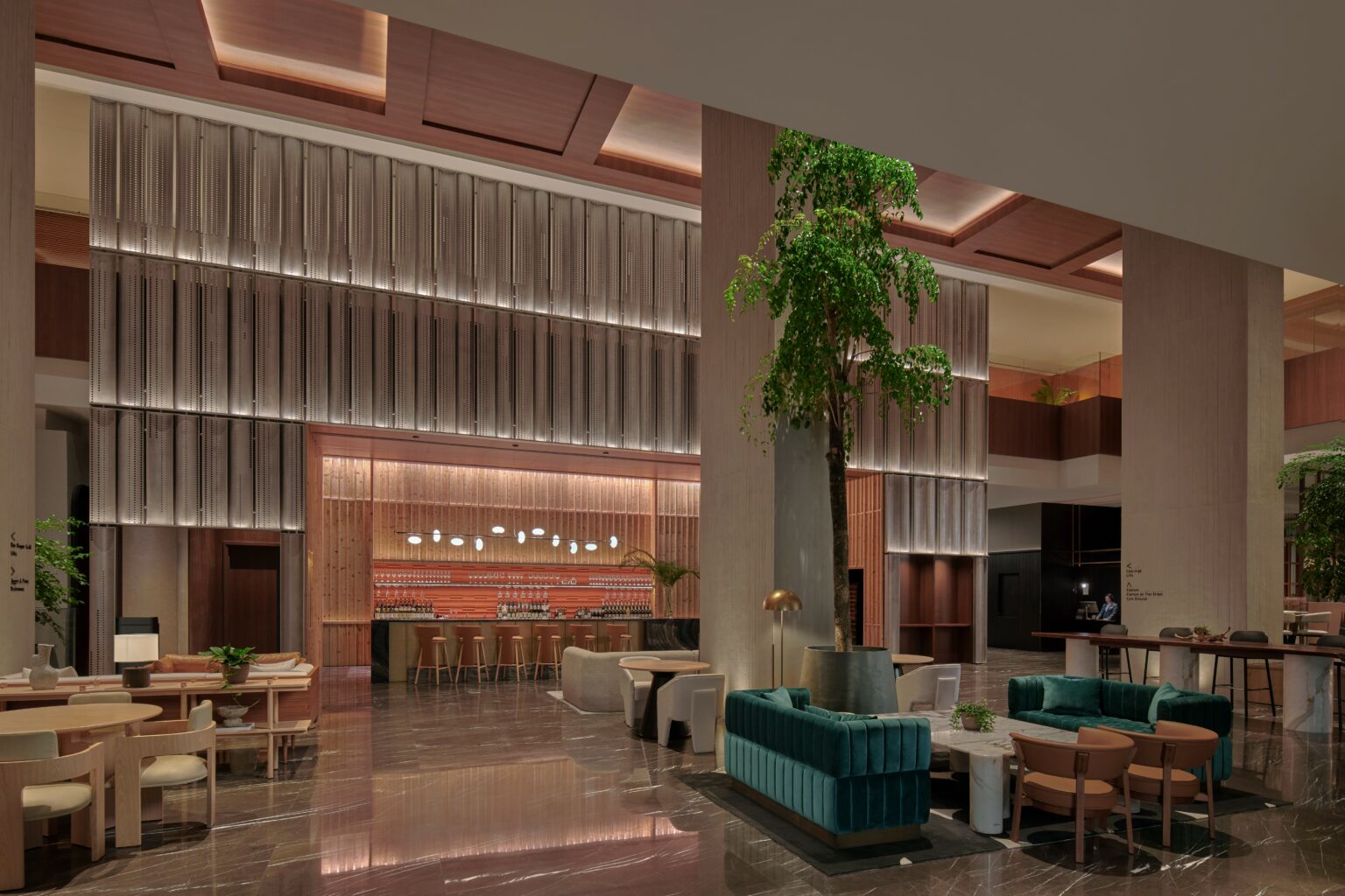 Luxurious hotel lobby with modern design, featuring high ceilings, plush seating, a central large plant, and a stylish bar at the back. Warm, inviting ambiance.