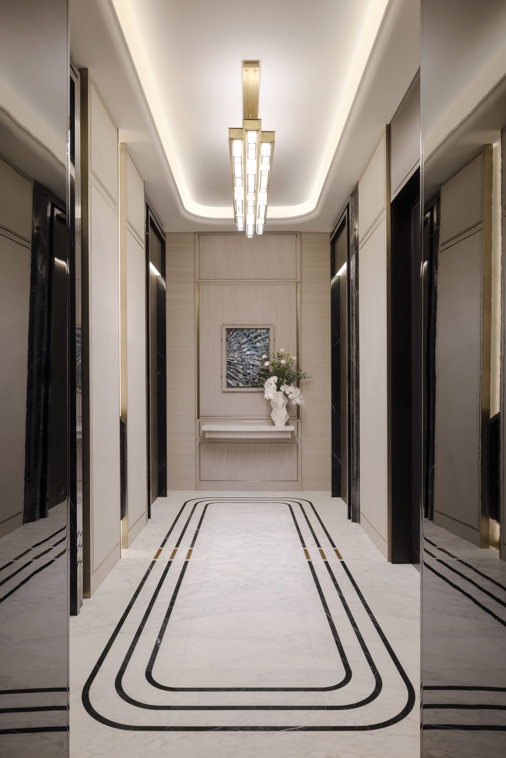 Elegant hallway of Waldorf Astoria Residences Dubai with soft lighting, featuring symmetrical elevator doors, a modern chandelier, and a floral arrangement on a console table.