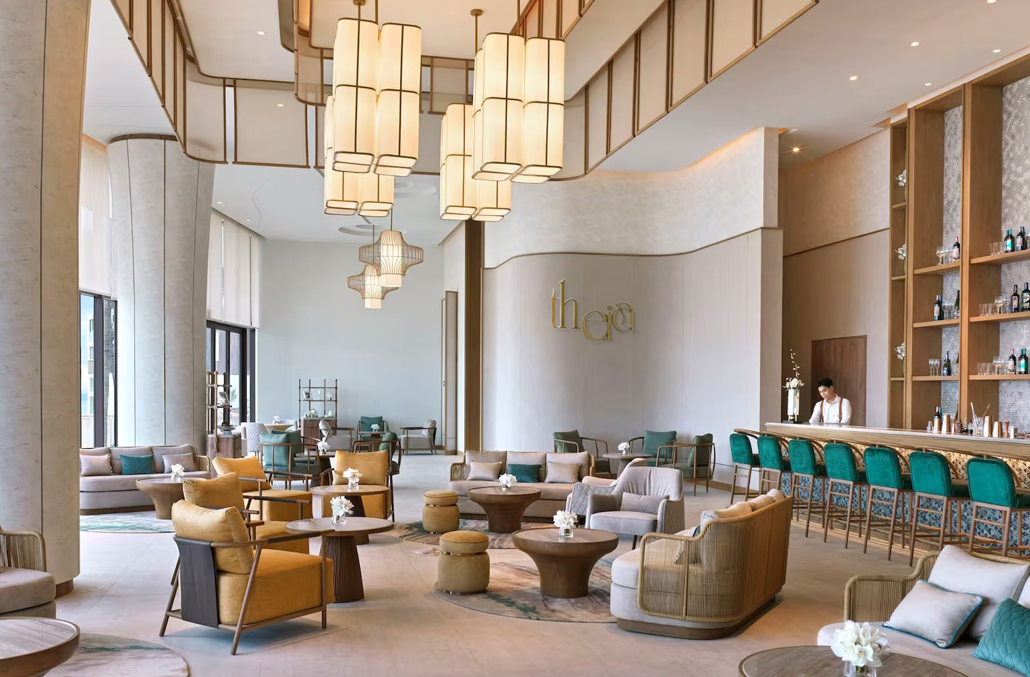 Luxurious, airy hotel cafe with ocean view. Features wicker chairs, green bar stools, potted plants, modern decor, and a server arranging items.